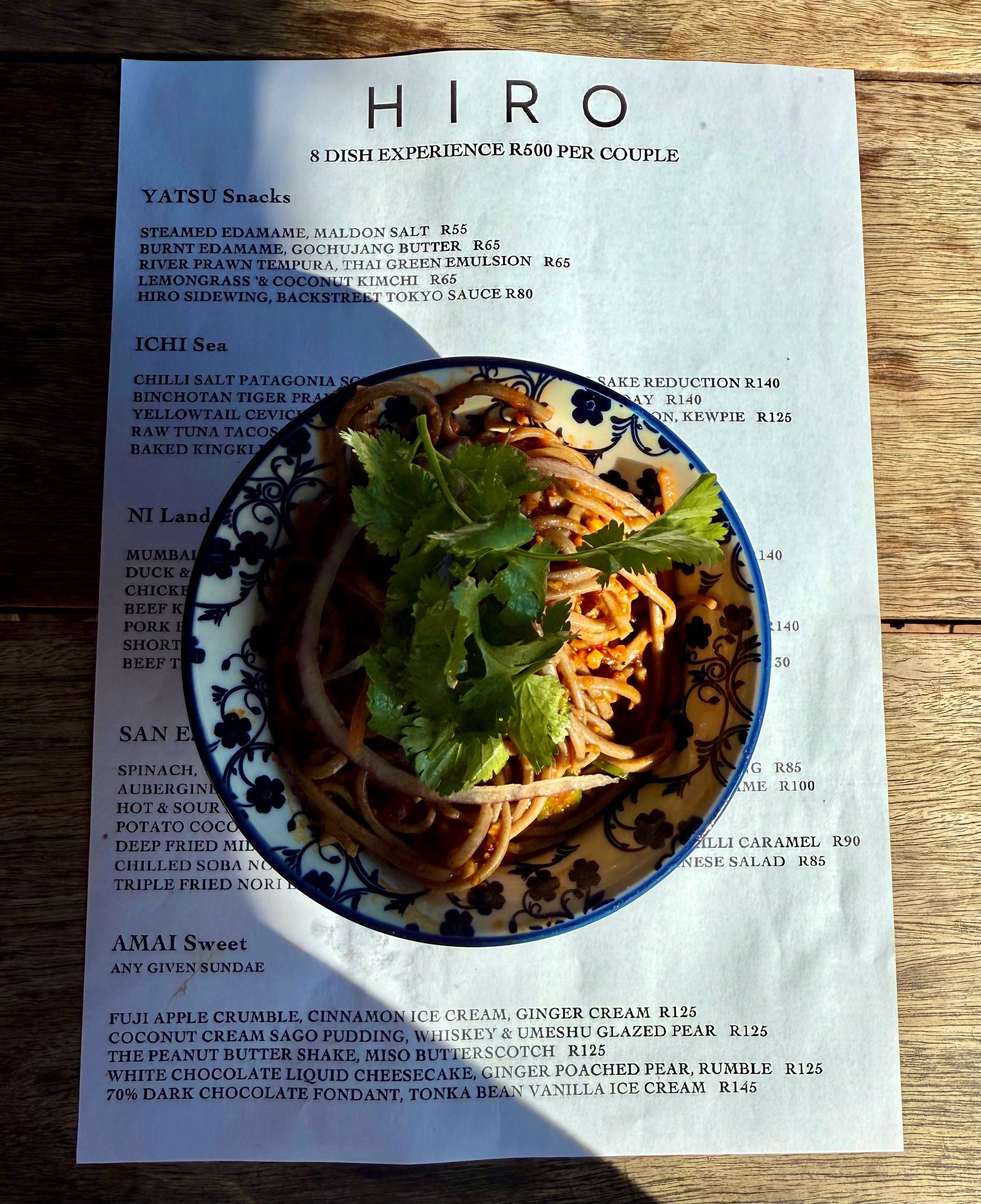 Bowl of noodles with cilantro and onions on a menu on a wooden table.