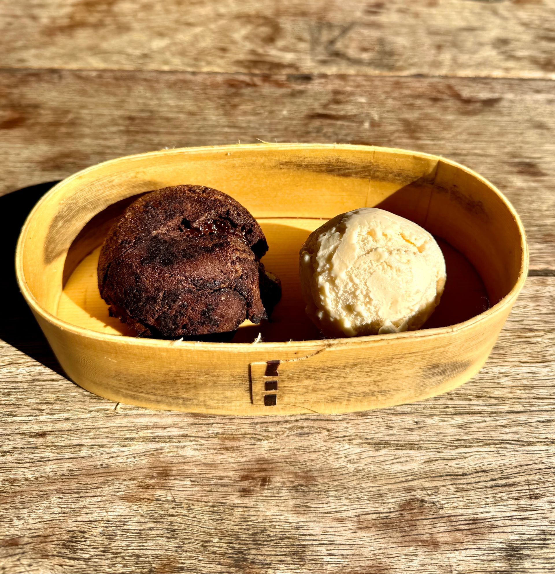 Two scoops of ice cream, chocolate and vanilla, in a yellow wooden oval dish on a wood surface.