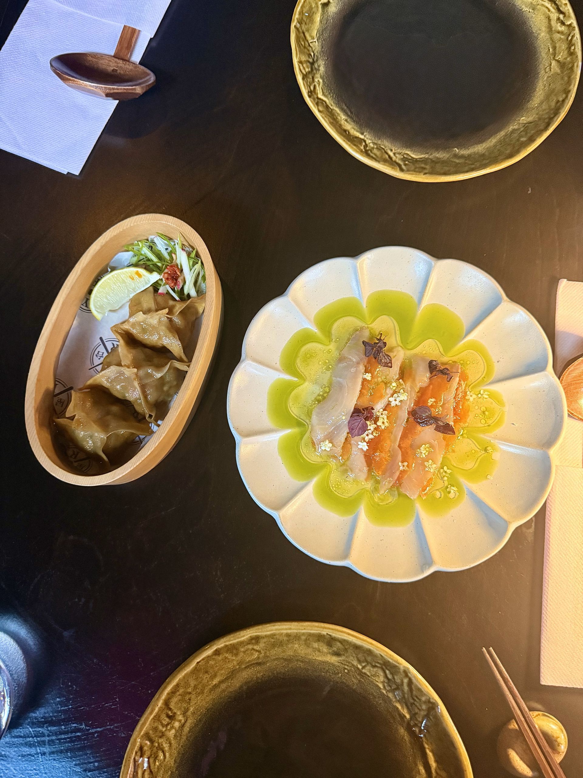 Dumplings and sashimi on decorative plates, arranged on a dark table.