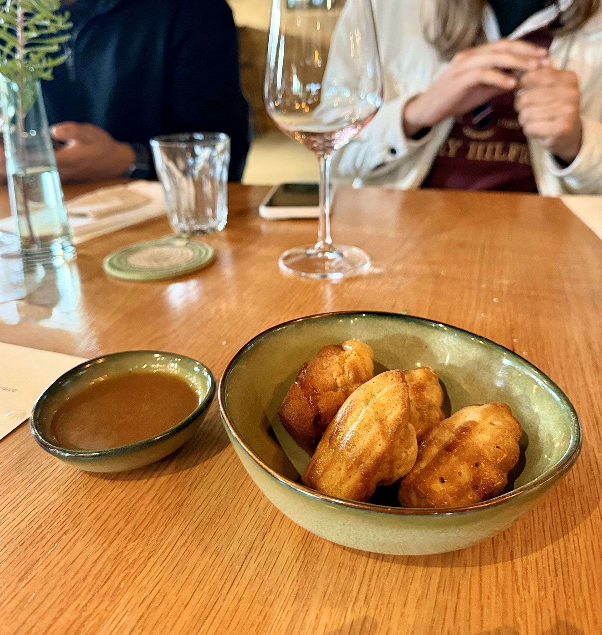Madeleines and sauce in bowls on a wooden table at a restaurant.