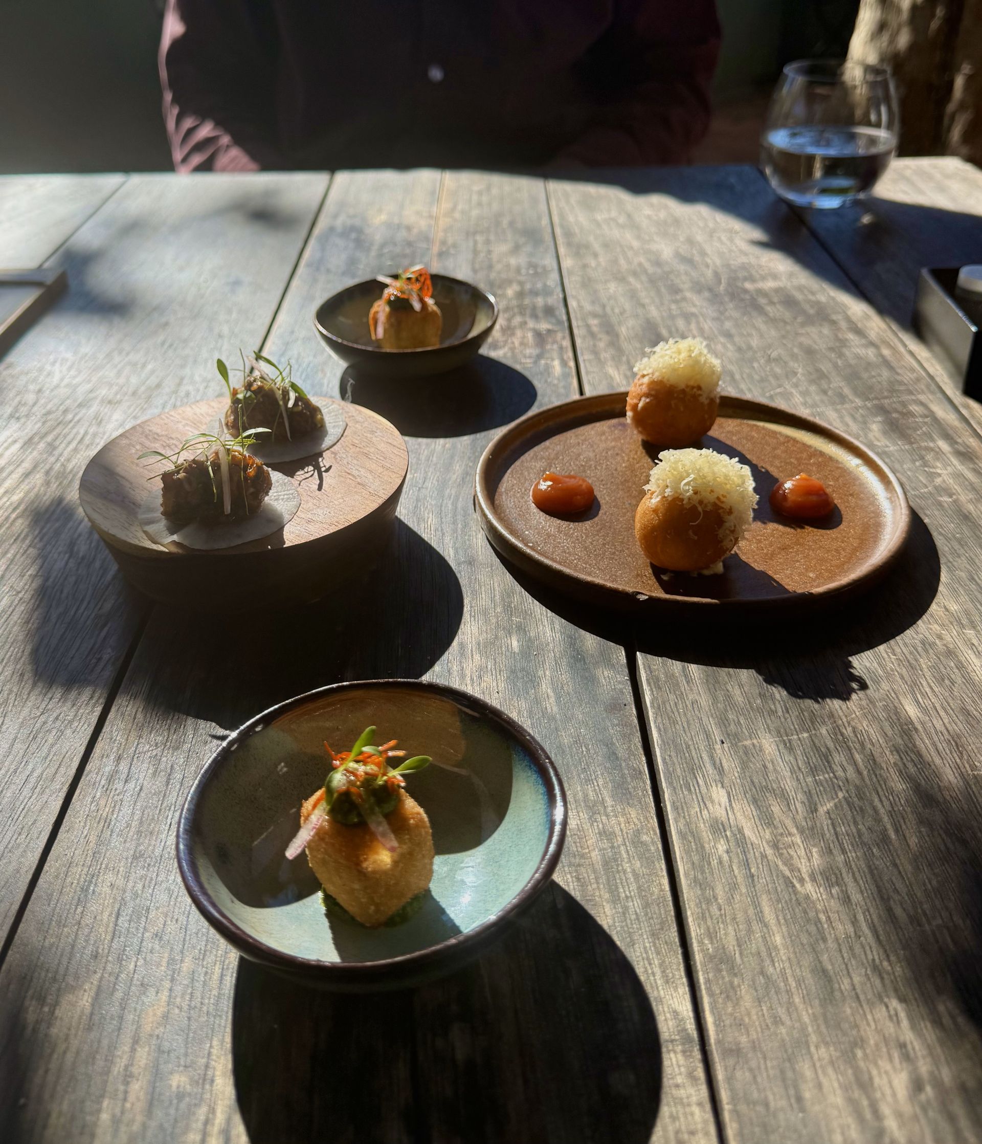 Four small dishes with appetizers on a rustic wooden table.