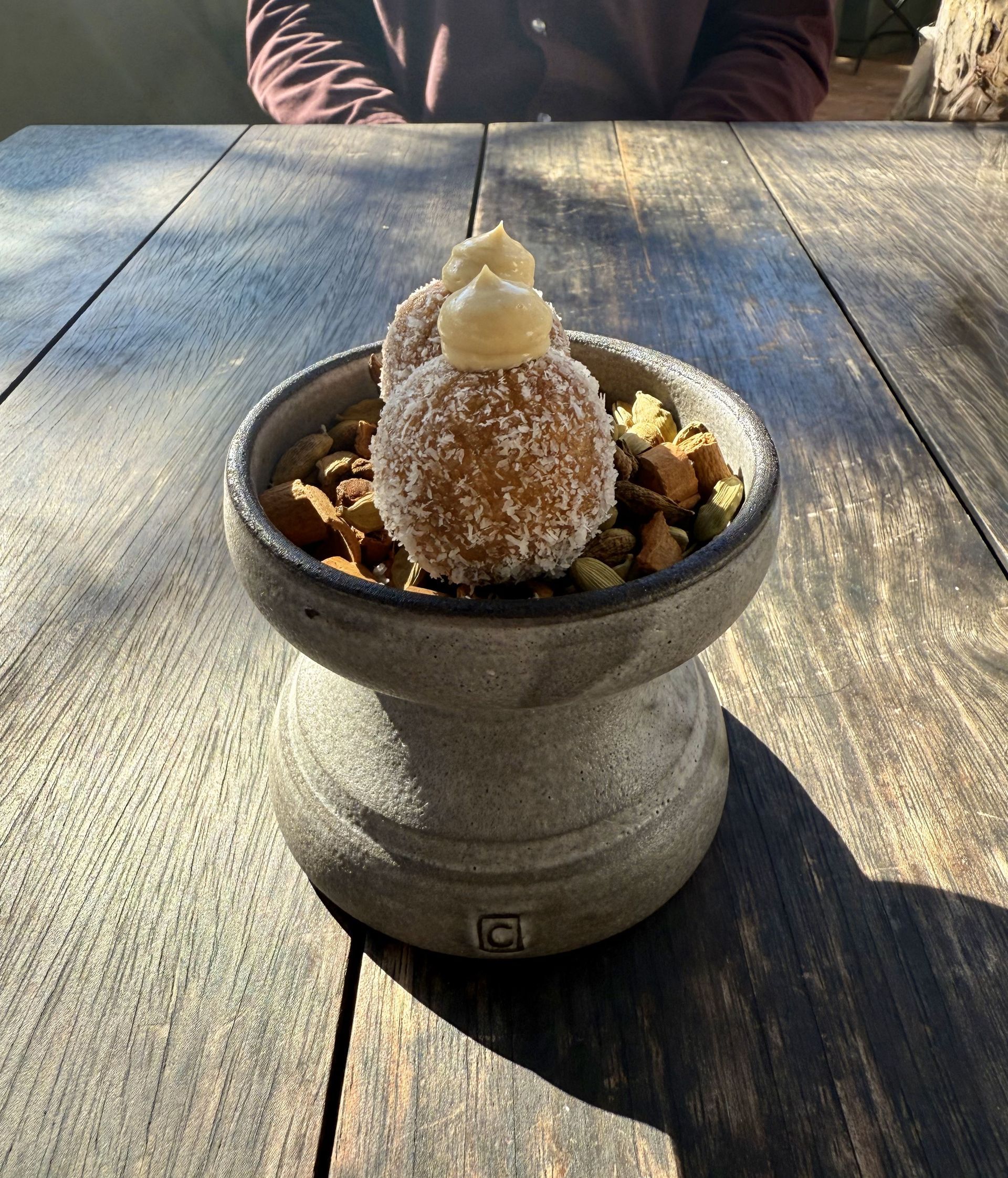 Coconut-crusted dessert balls topped with cream, in a stone bowl atop a weathered wooden table.