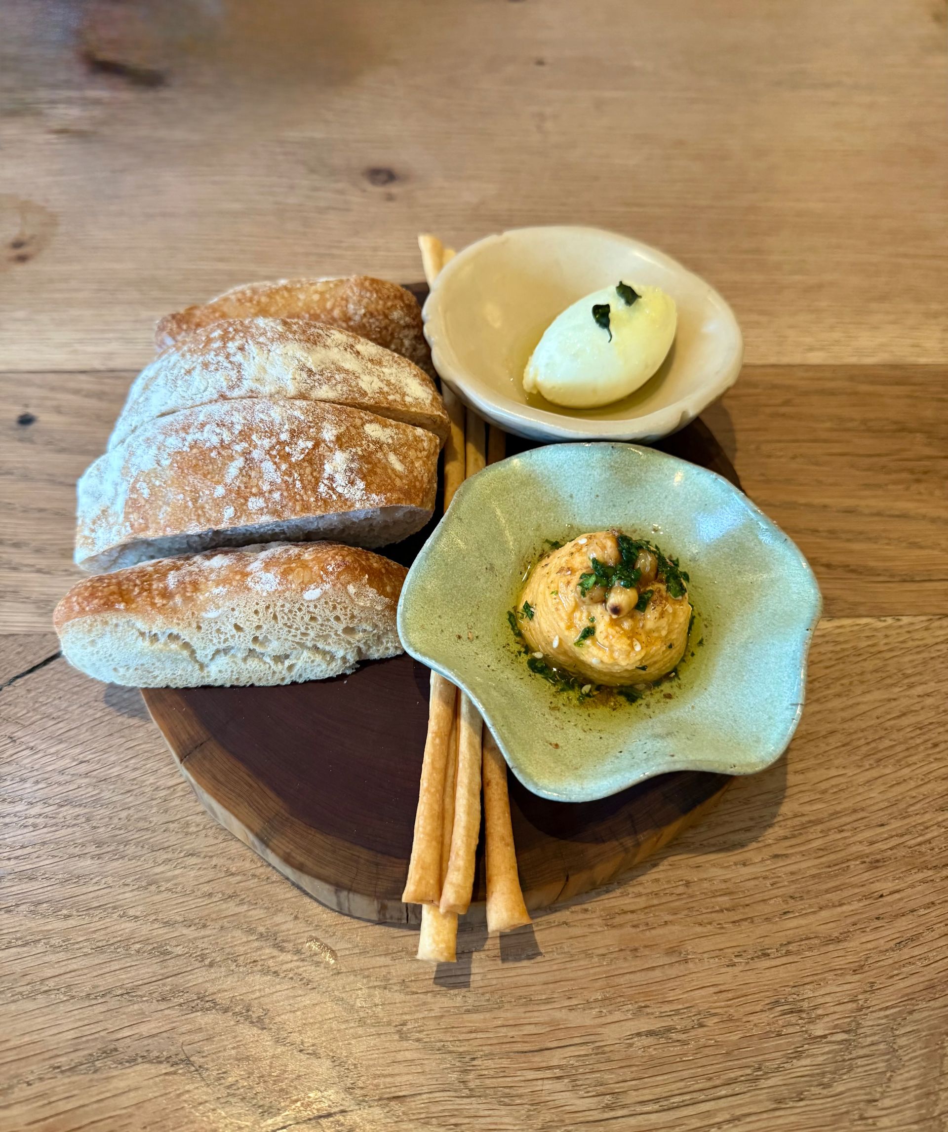 Bread slices, breadsticks, and butter served on a wooden platter.