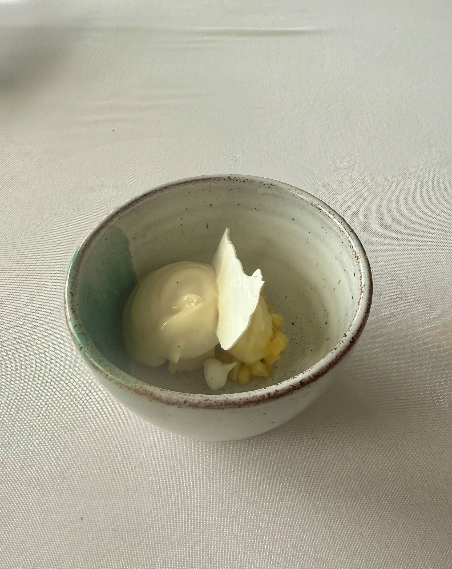 Small bowl of pale yellow dessert with white garnish, set on a patterned white tablecloth.