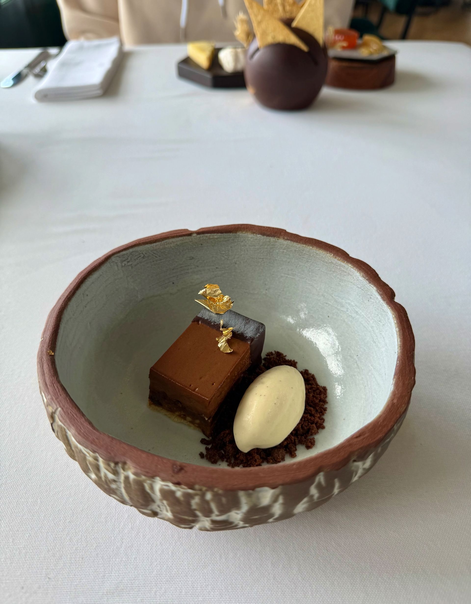 Chocolate dessert with ice cream and crumble in a rustic bowl on a white table.
