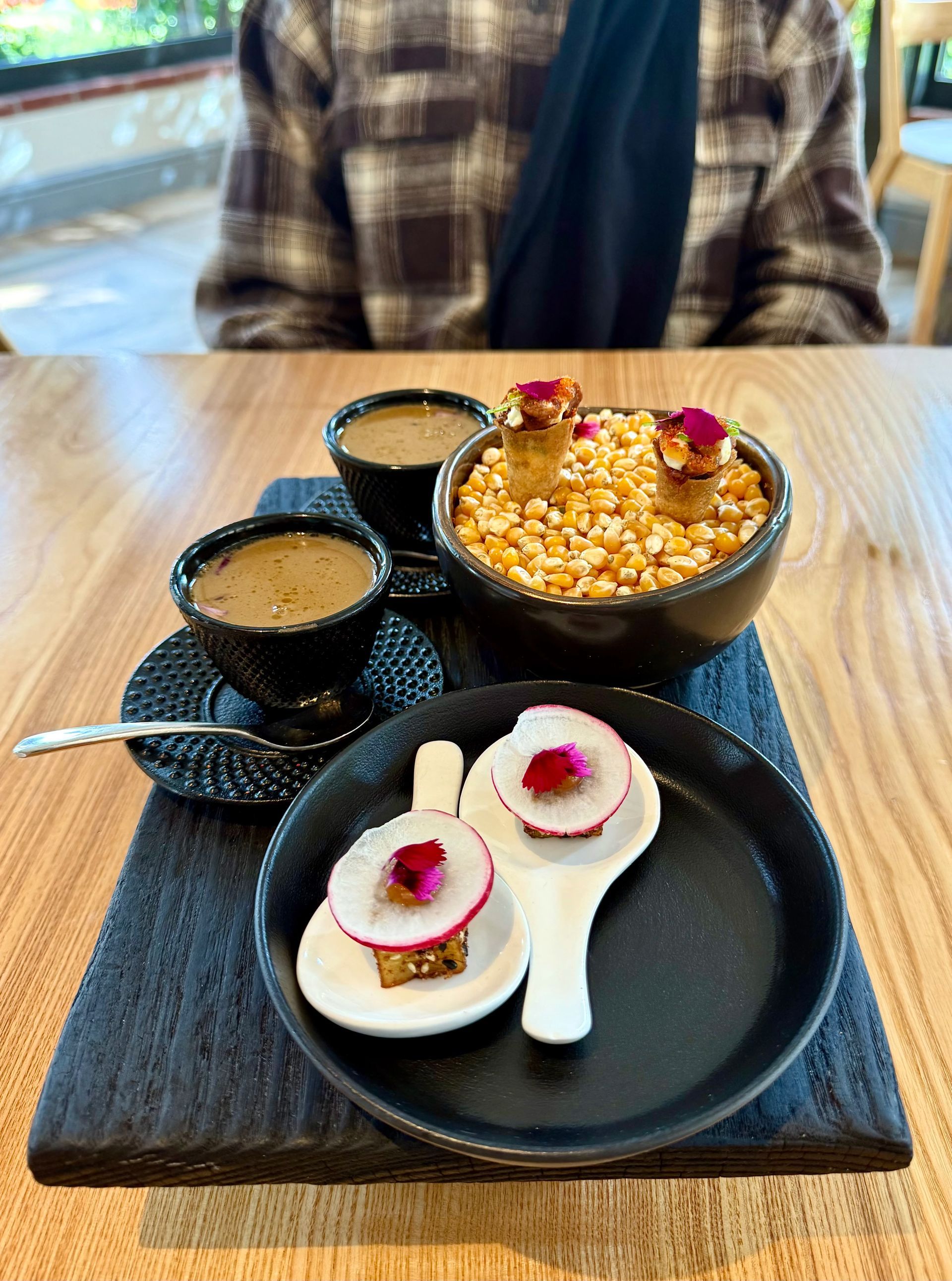 A small plate with appetizers and coffee cups on a wooden table; a person in the background.
