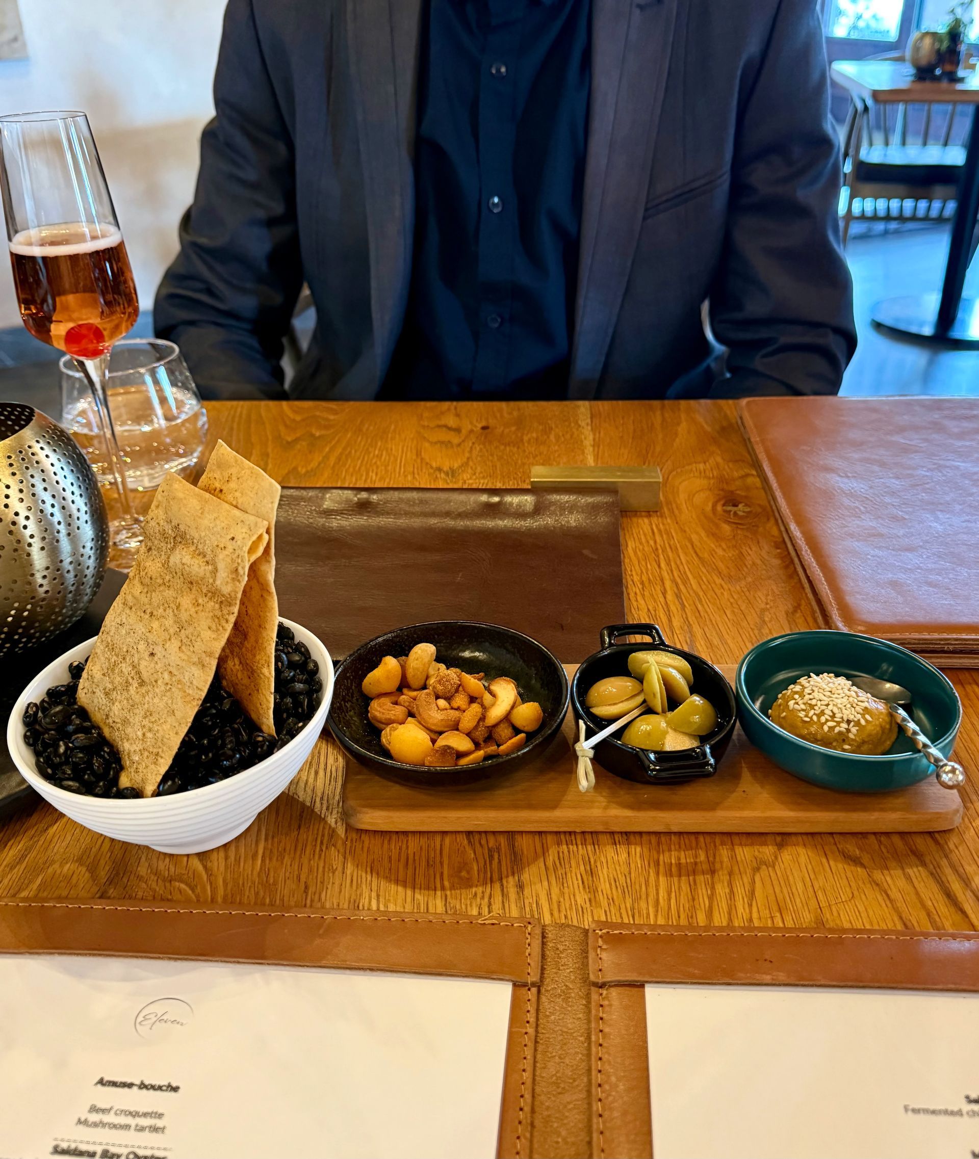 Person at a table with snacks and a drink, in a restaurant setting.