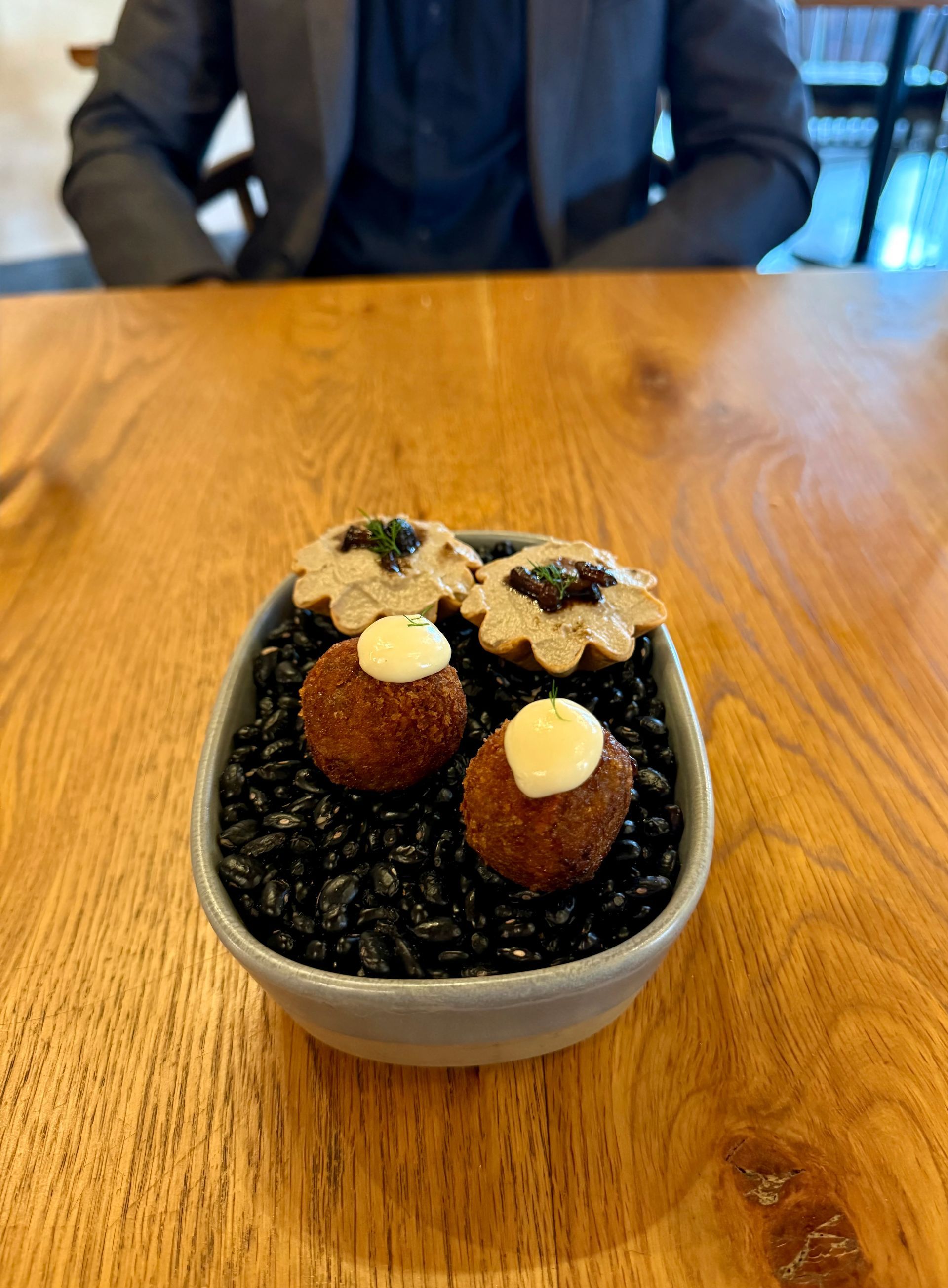 Small bowl with croquettes and mushroom pastries on black beans, on a wooden table.
