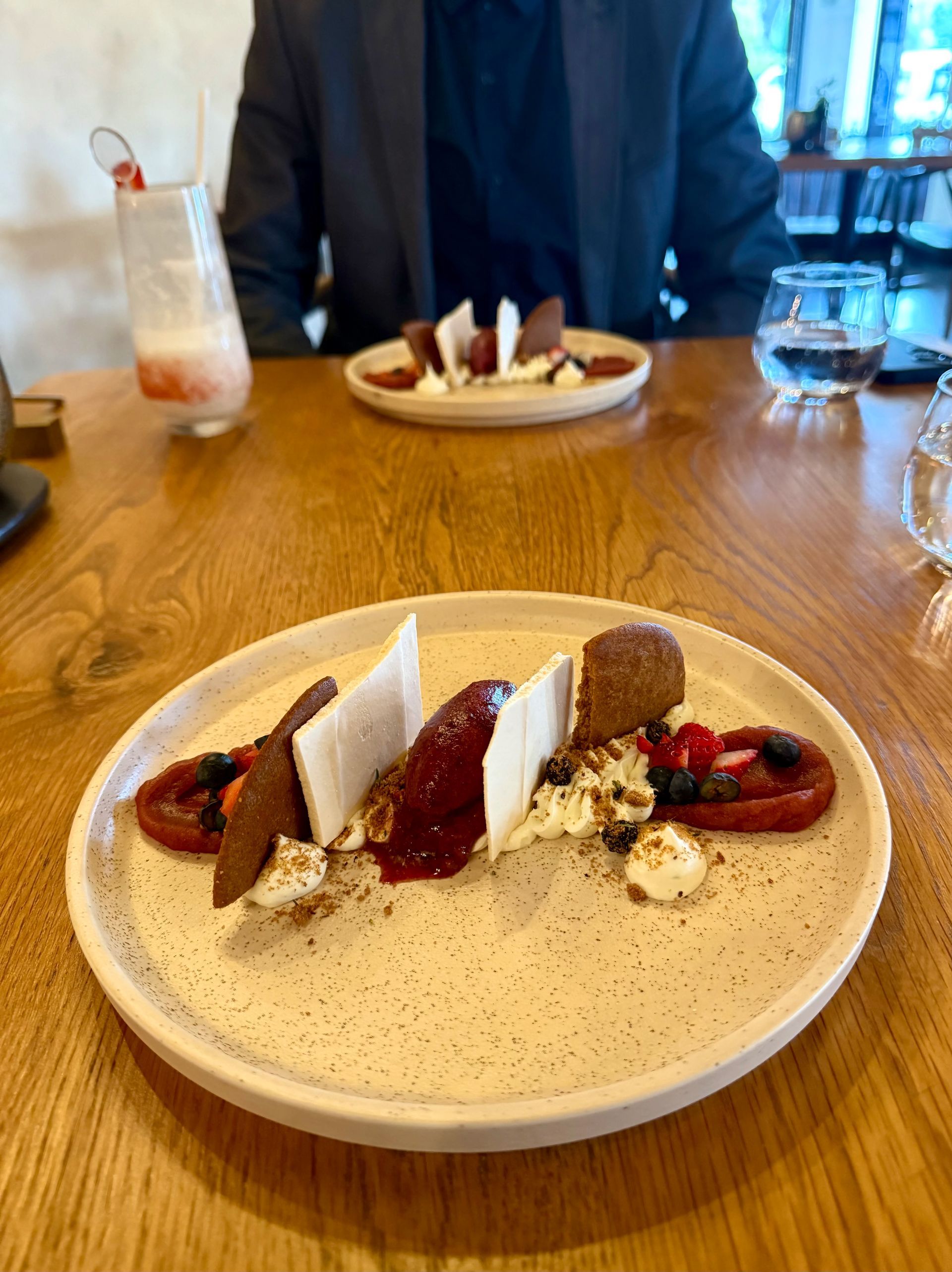 Dessert plate with strawberries, chocolate, and whipped cream on a wooden table, a person in background.
