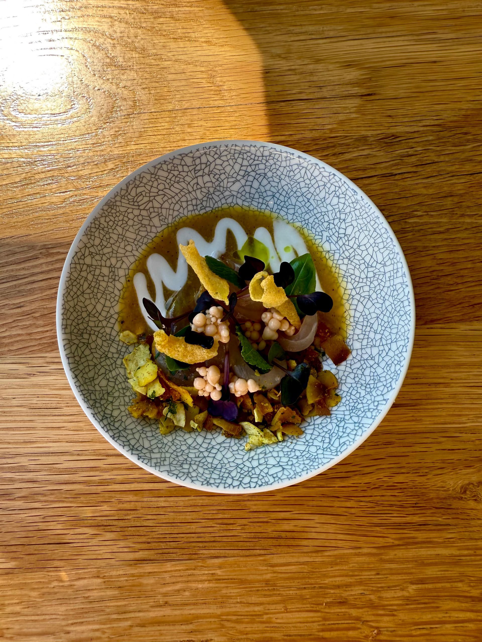 Close-up view of a colorful plated dish with various ingredients and garnishes on a wooden table.