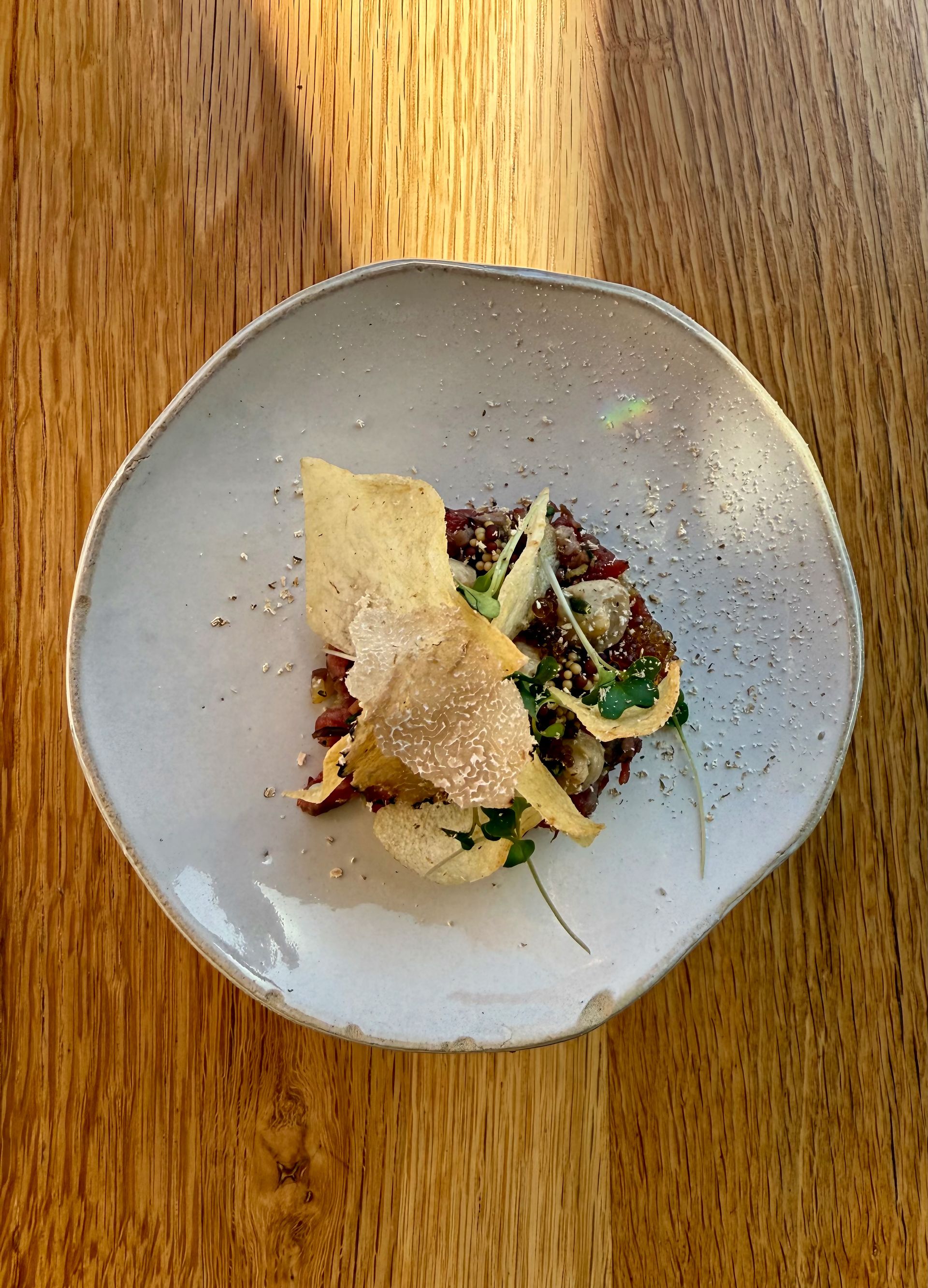 Dish on a light-colored plate with chips and herbs on a wooden table.