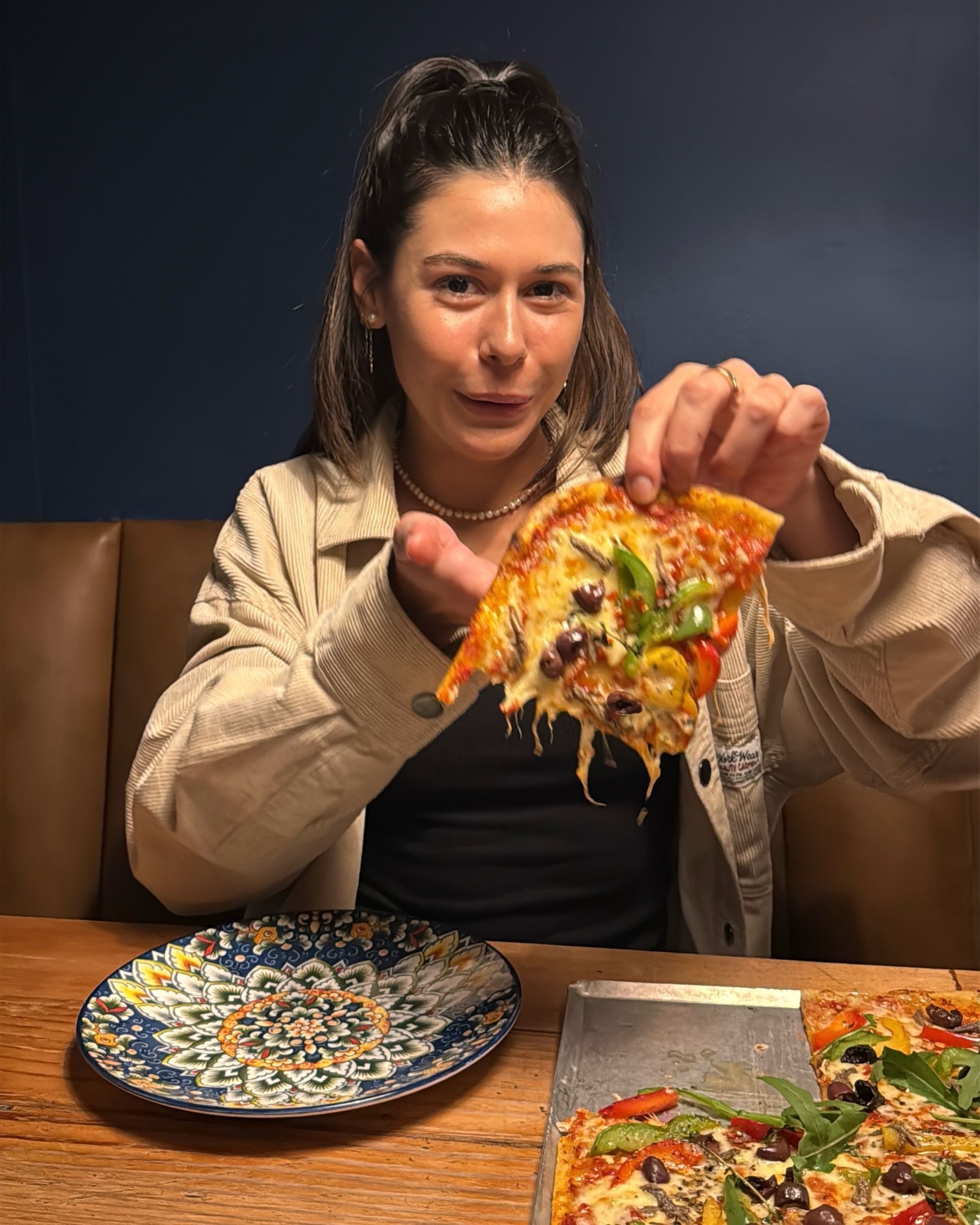 Paige holding a slice of thin crust sheet pan-style pizza at Jerry’s
