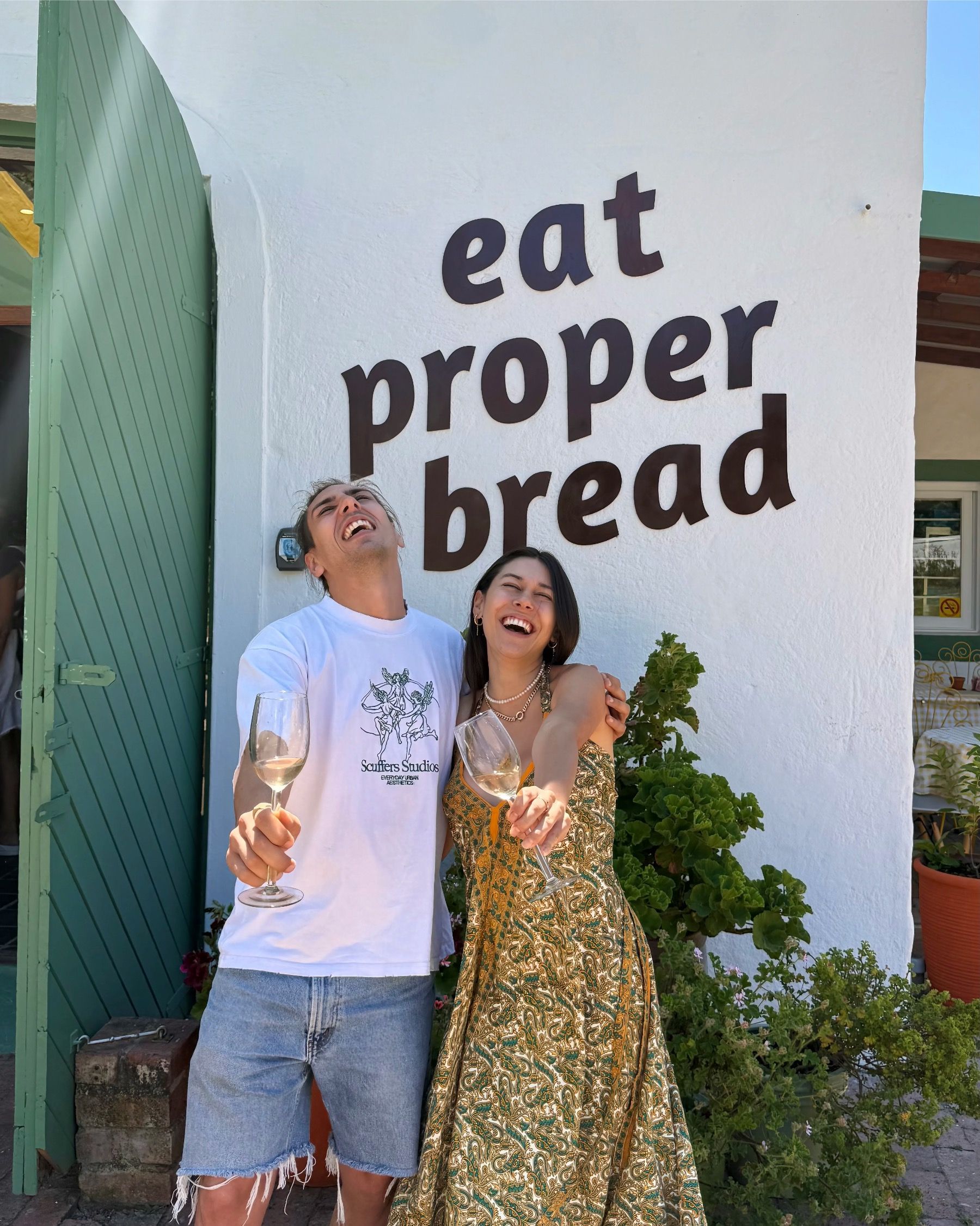 Paige at the Motherdough Jonkershoek launch with a glass of bubbly in front of the “Eat Proper Bread” sign in Stellenbosch