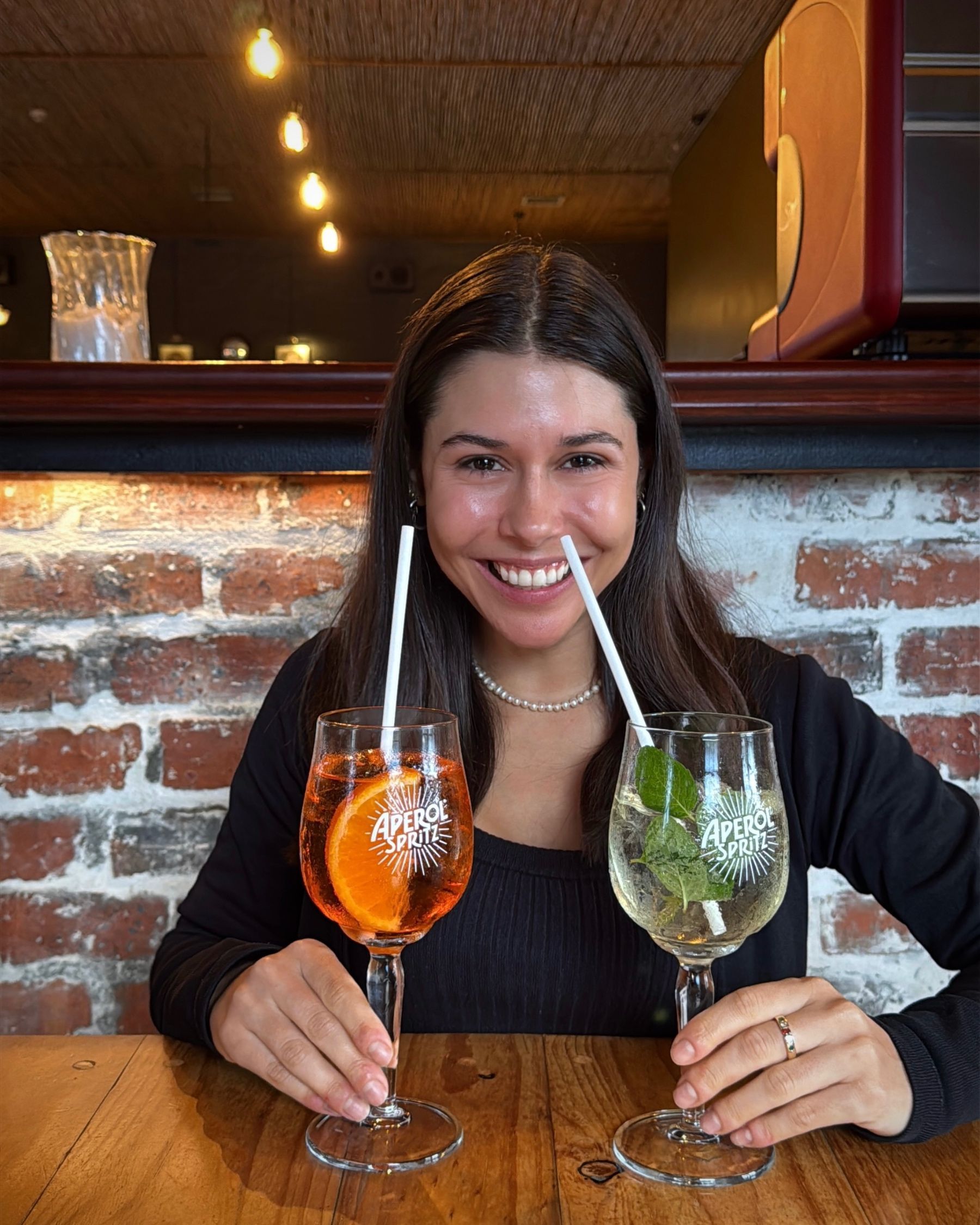 Paige smiling while holding a Hugo Spritz and an Aperol Spritz.
