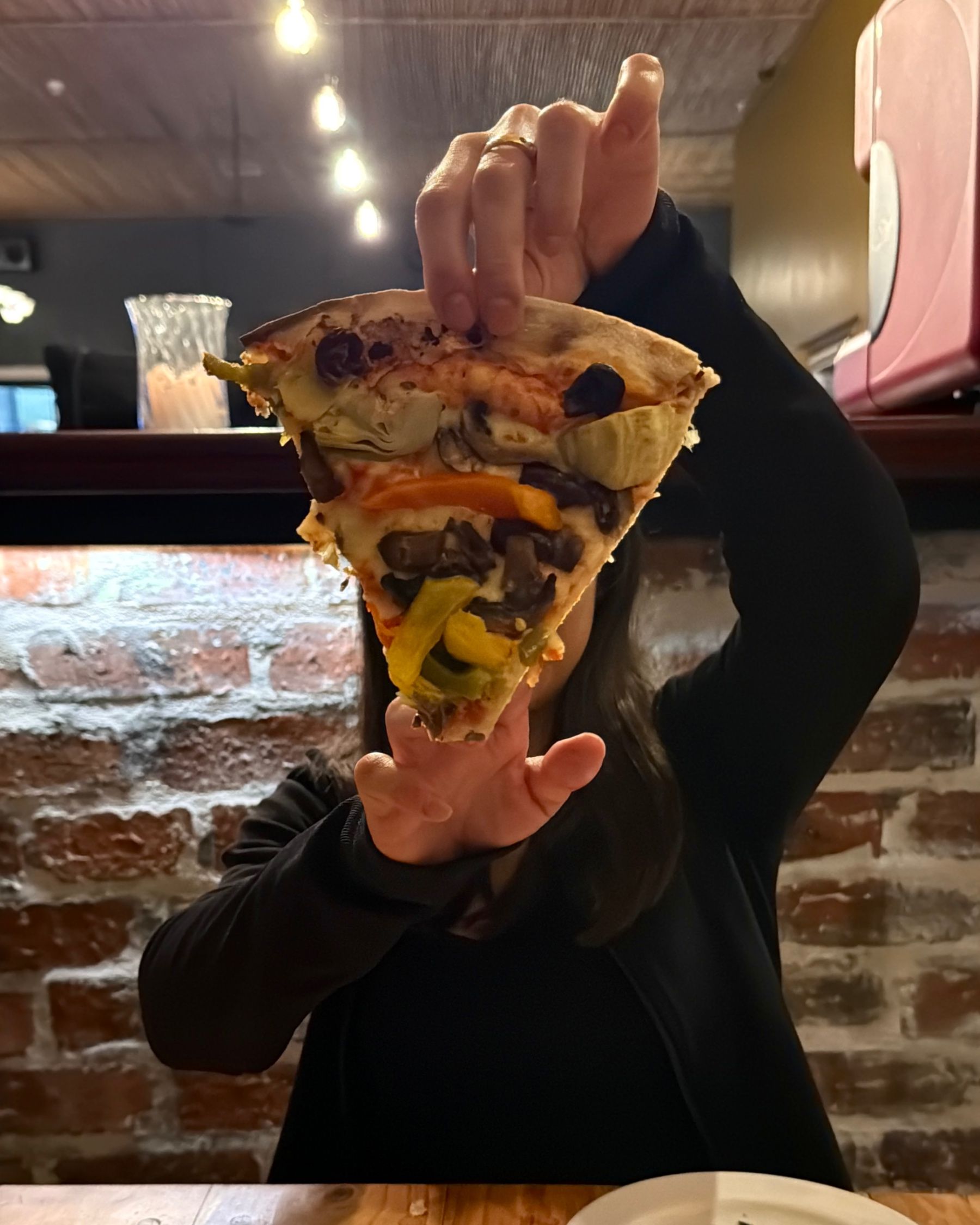 Paige holding a slice of vegetarian pizza towards the camera.
