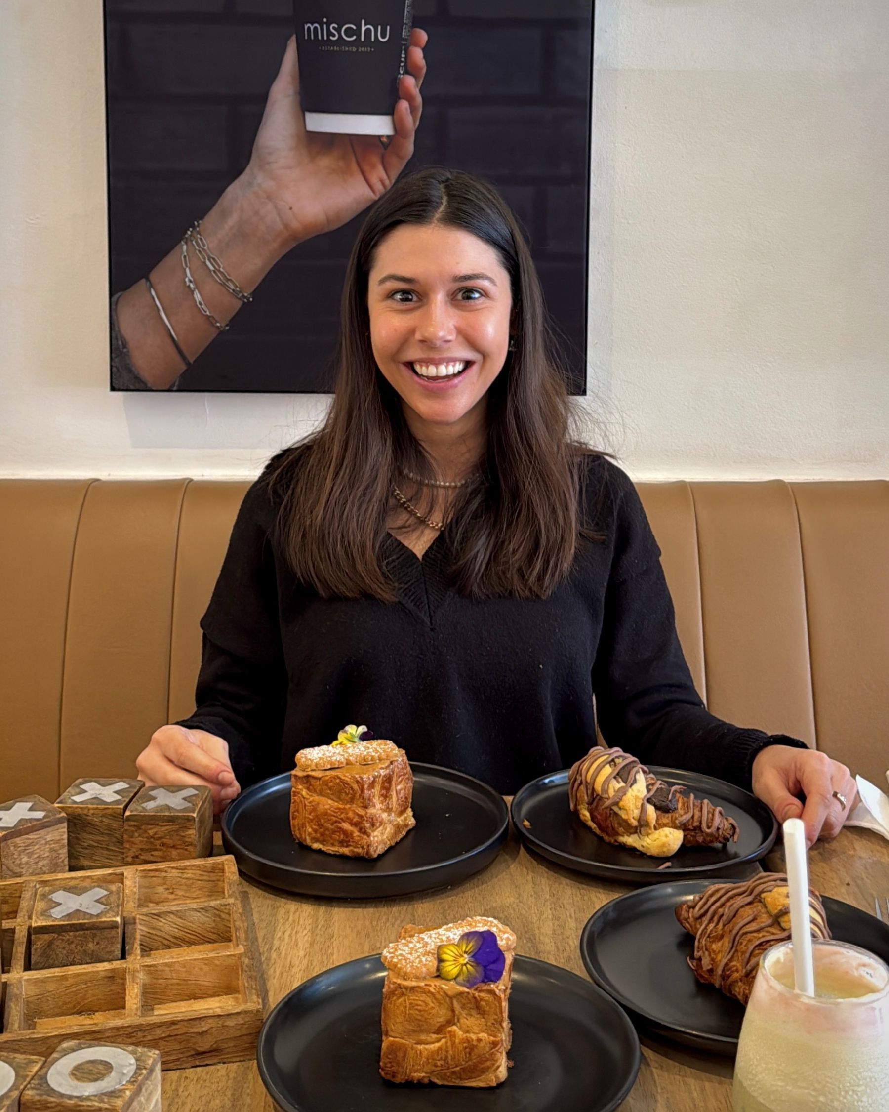 Paige smiling with noughts and crosses and a selection of Mischu pastries on the table.
