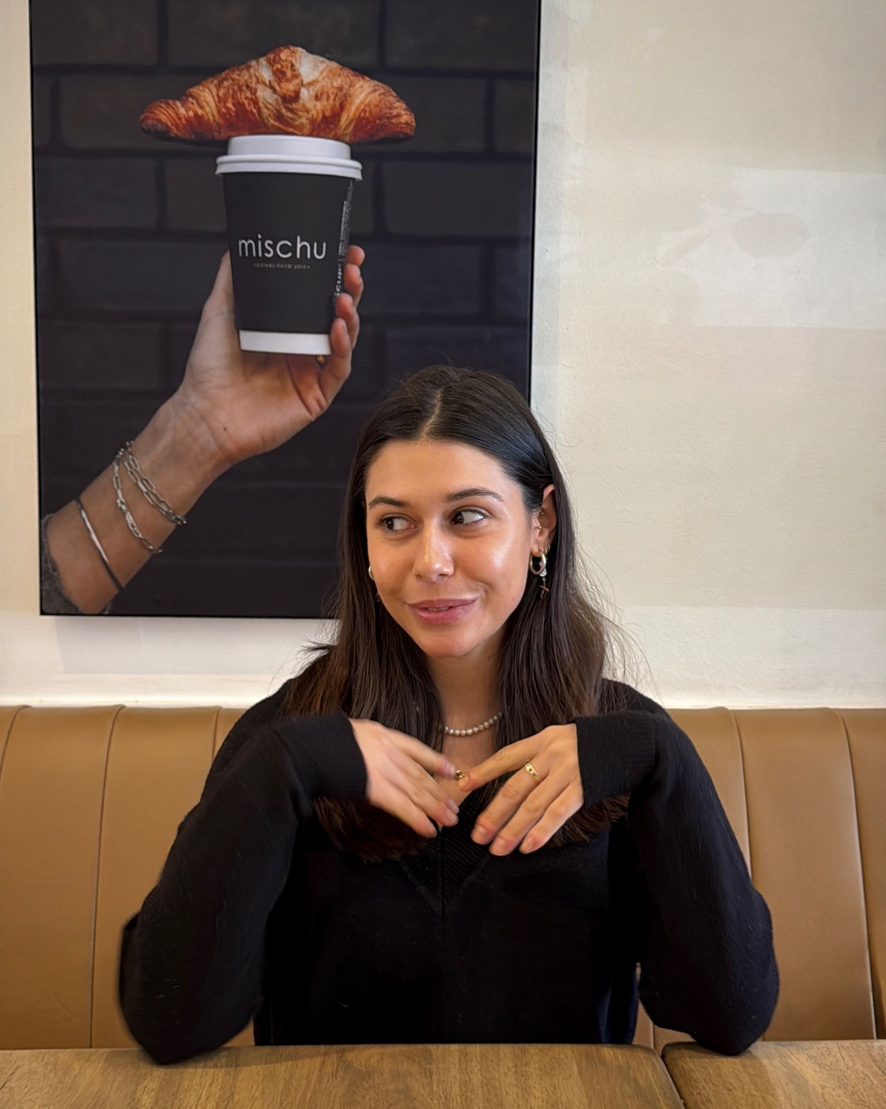 Paige seated inside Mischu with the café’s coffee cup artwork behind her.