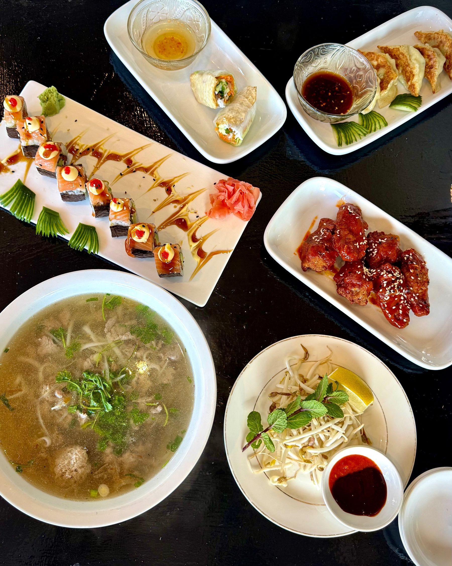 An overhead spread of chicken dumplings, fresh spring rolls, Korean fried chicken wings, beef pho and salmon rainbow rolls at Pho Hue.
