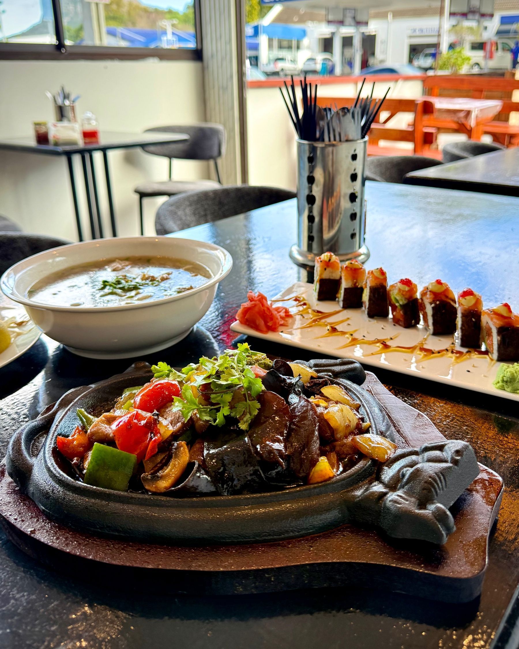 Sizzling beef stir fry with colourful vegetables served at Pho Hue, with beef pho and sushi in the background.