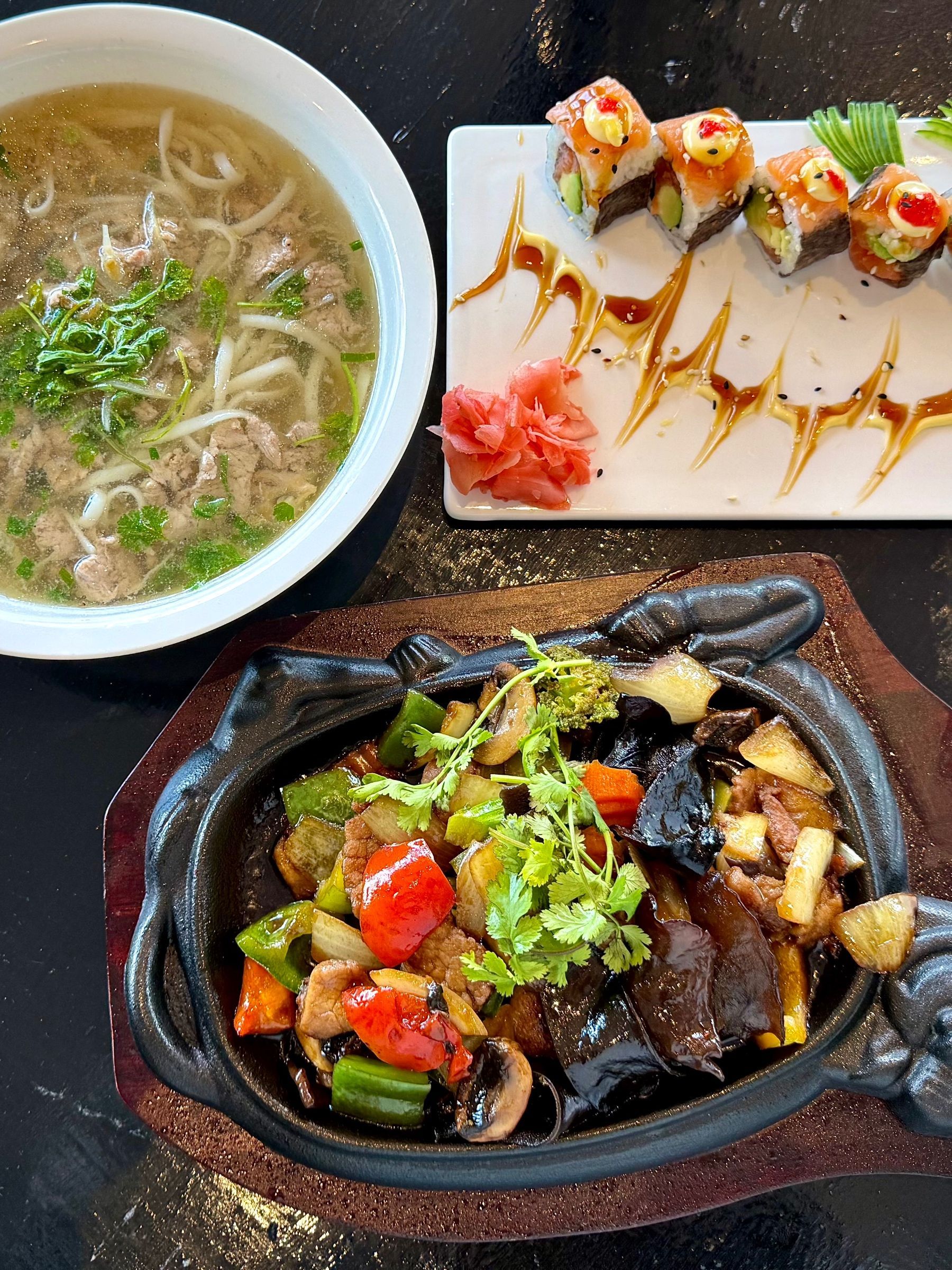 A spread of beef stir fry, beef pho and fresh salmon rainbow rolls at Pho Hue.