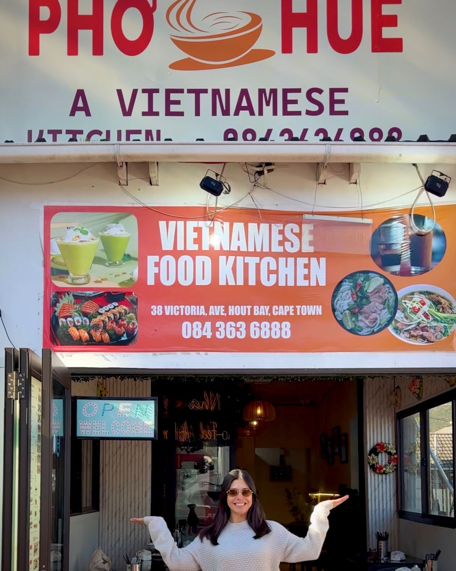 Paige smiling in front of the Pho Hue restaurant sign in Hout Bay, Cape Town.