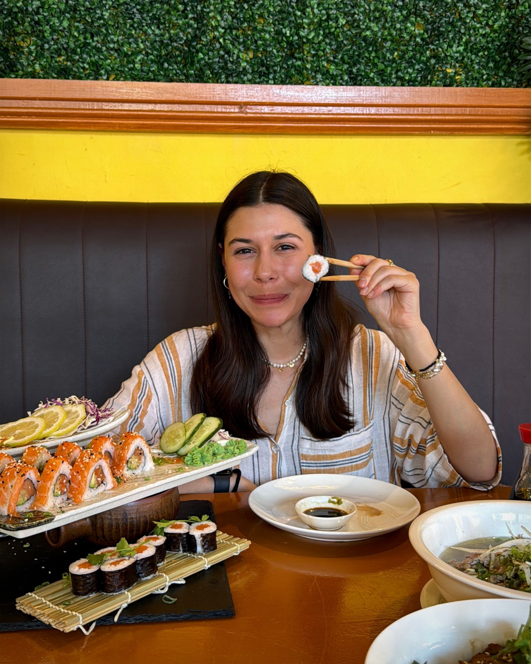 Paige smiling happily at the table after enjoying the sushi selection at Aiko Sushi Plus.