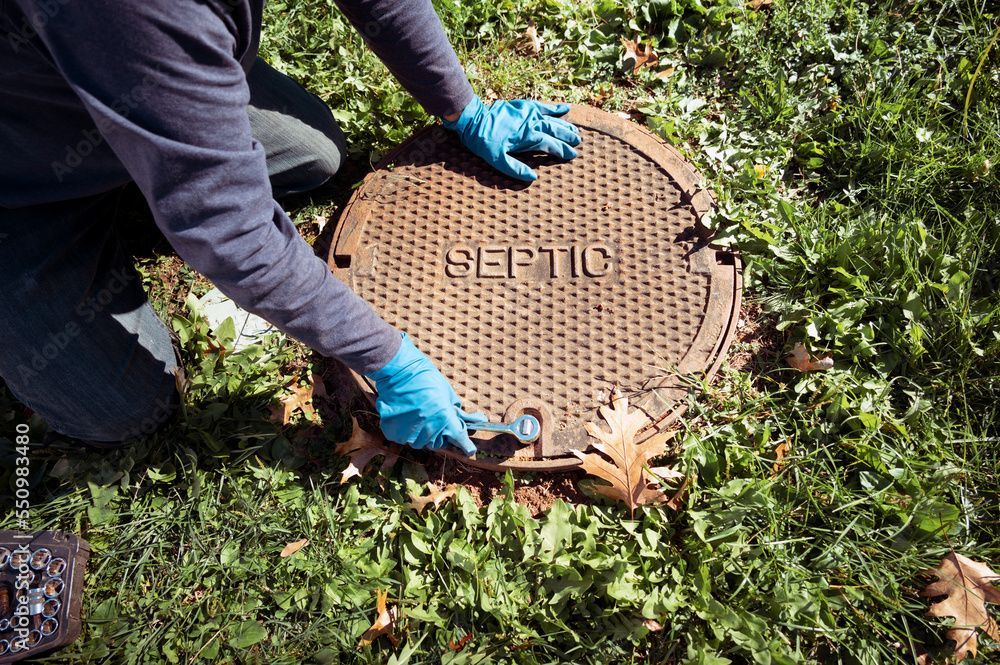 A person wearing blue gloves is opening a septic tank lid.