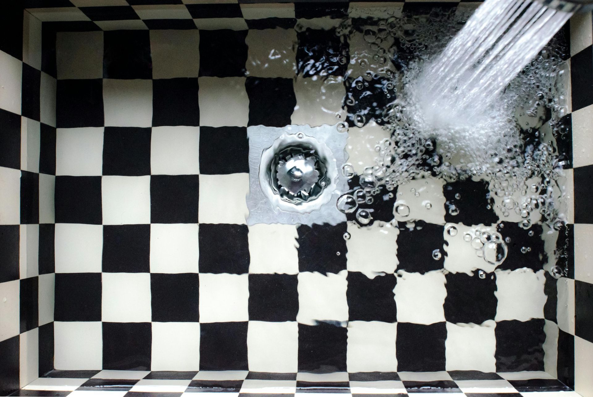 A black and white checkered floor with water coming out of the drain