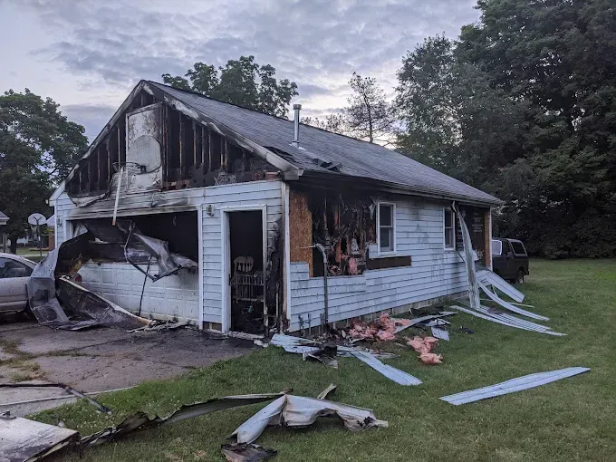 A house that has been damaged by a fire is sitting in the middle of a grassy field.