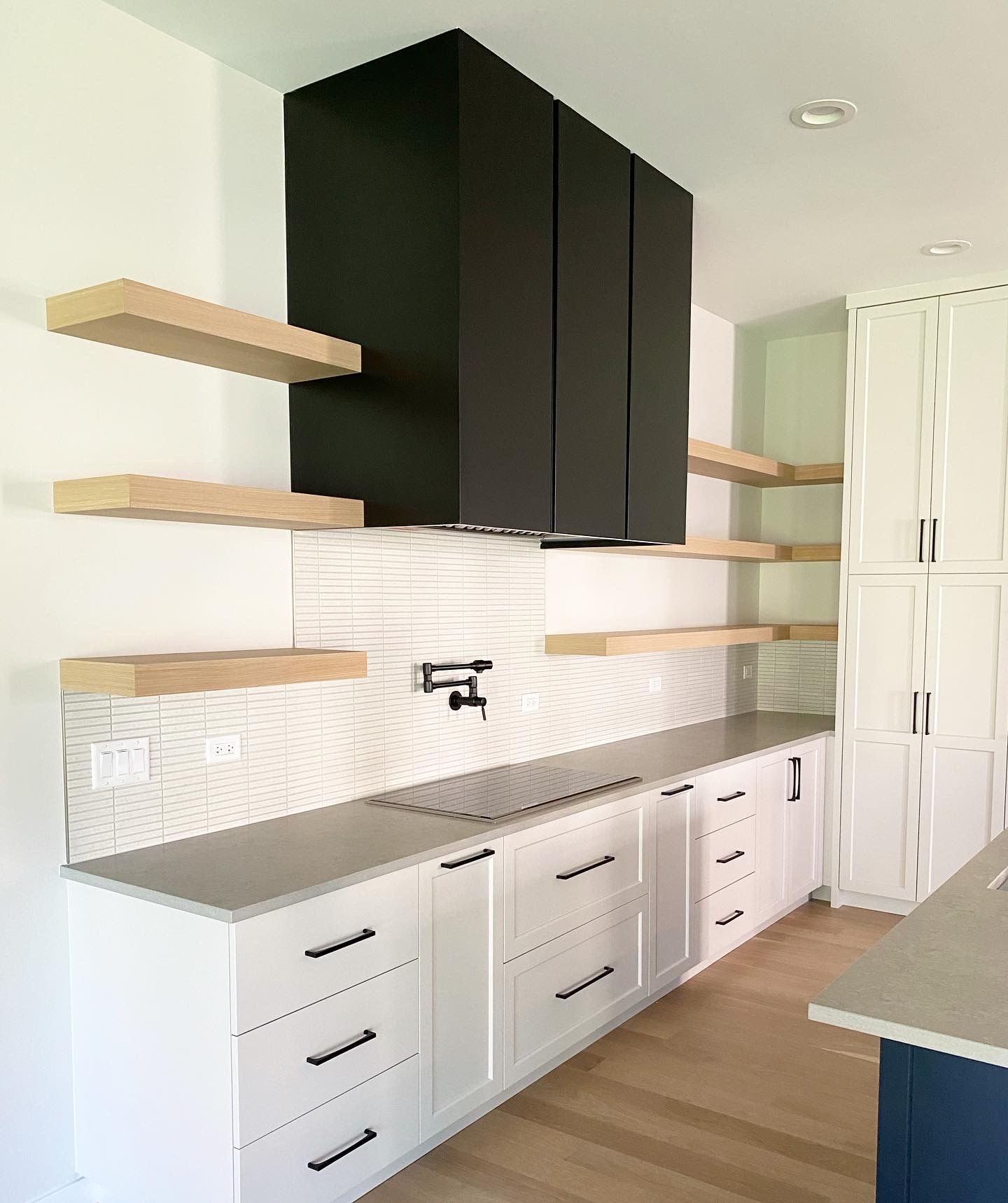 A kitchen with white cabinets , wooden shelves and a black hood.