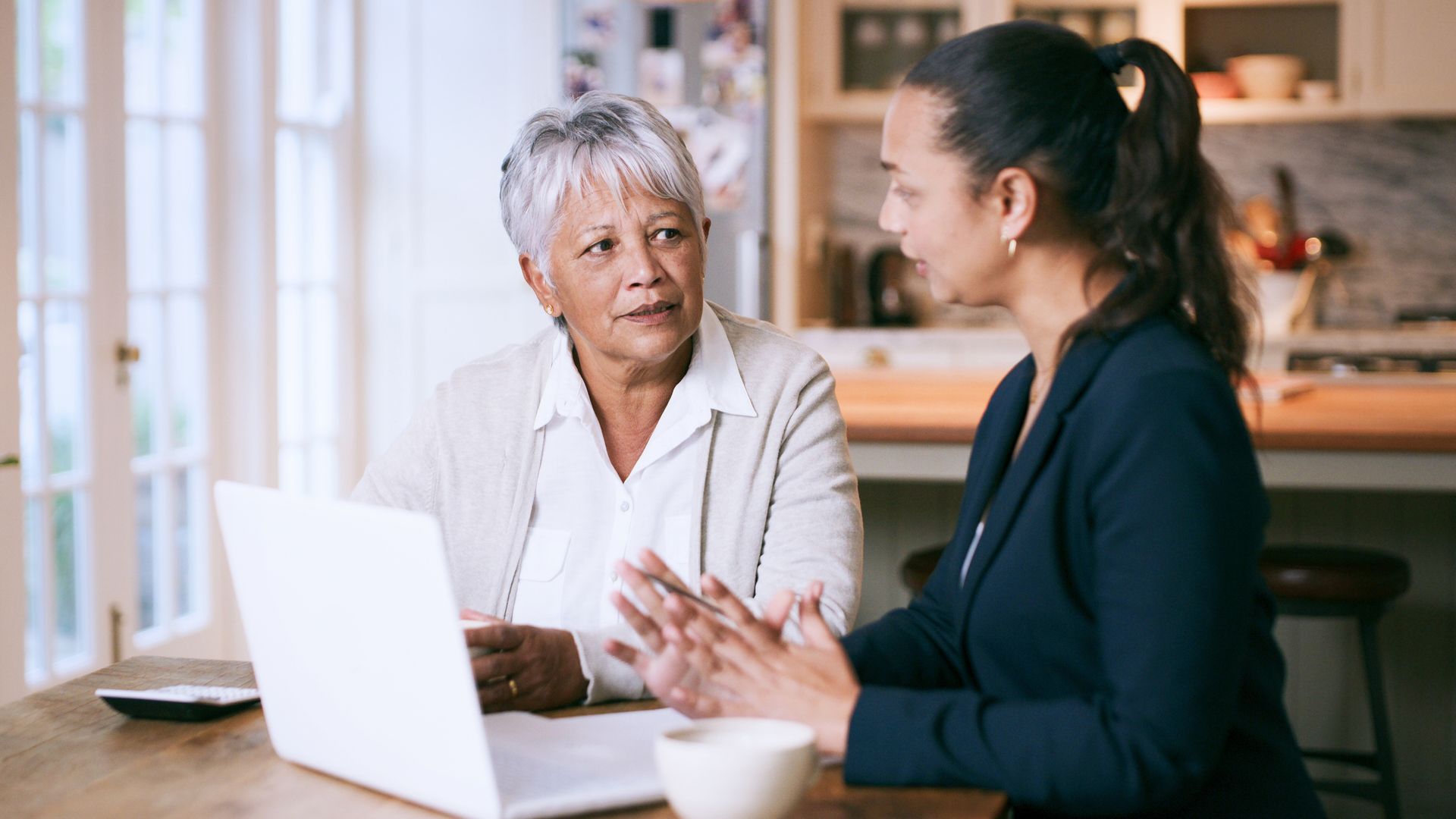 Two women are sitting at a table looking at a laptop computer.