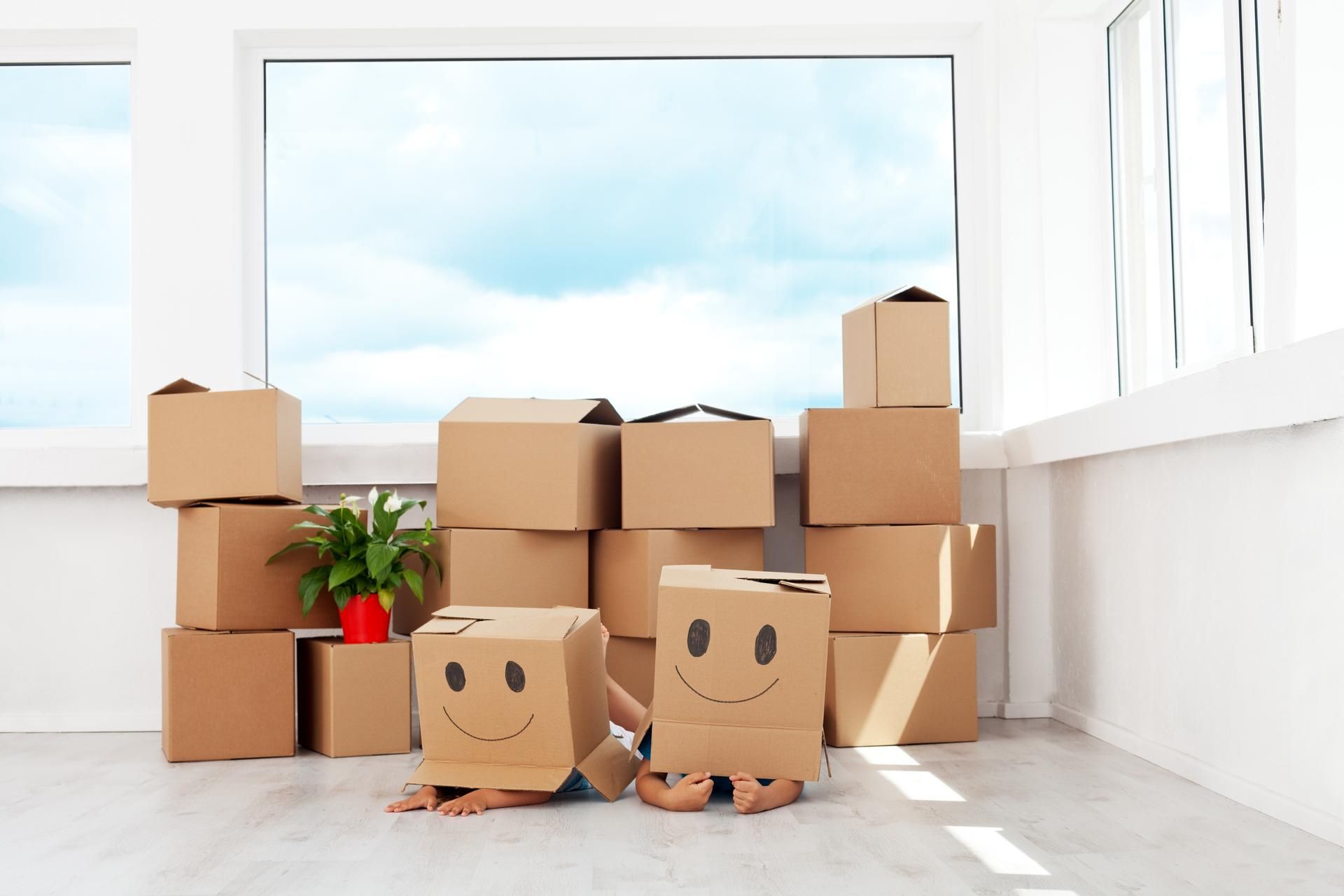 Two children are hiding behind cardboard boxes with smiley faces on them.