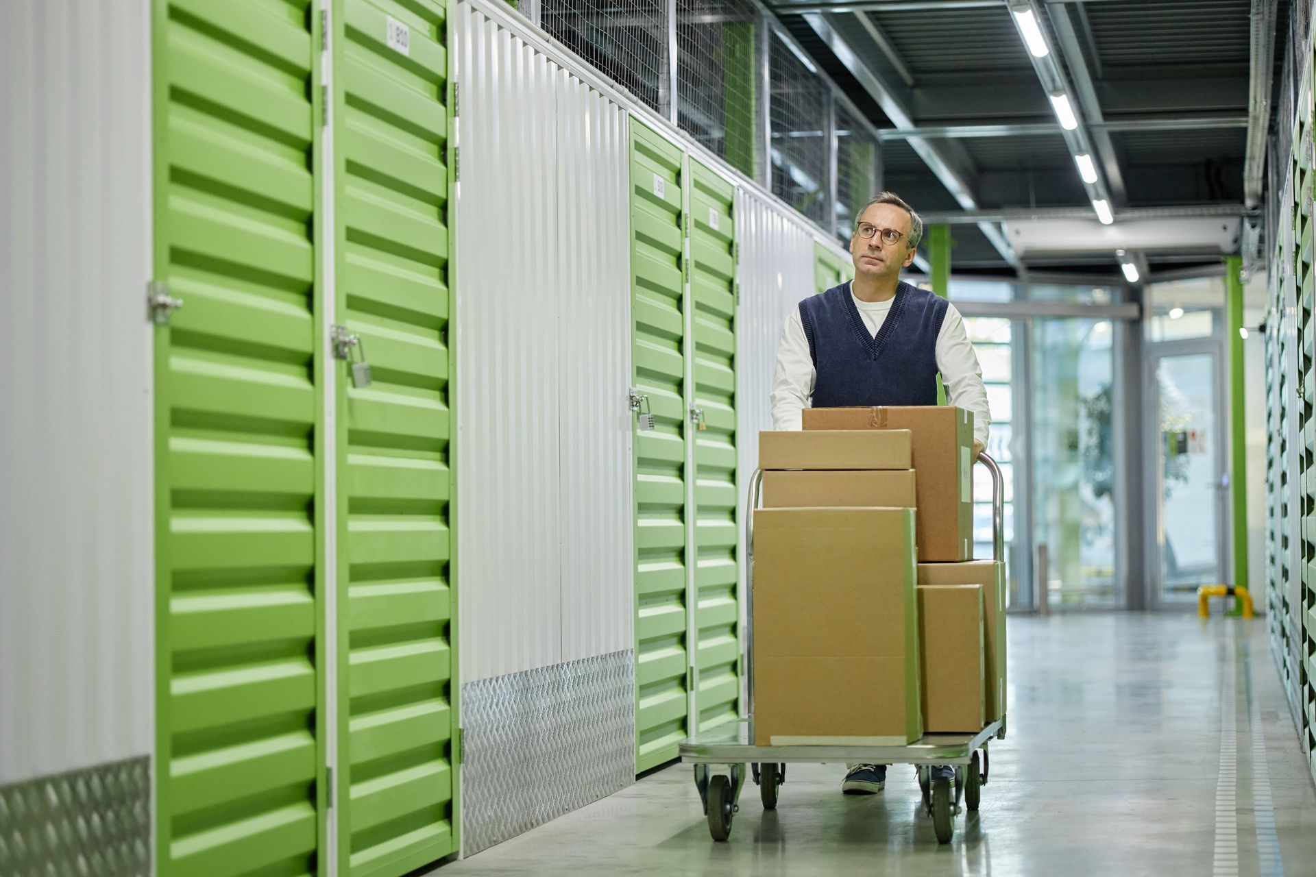 Worker moving boxes on a cart inside business storage units.