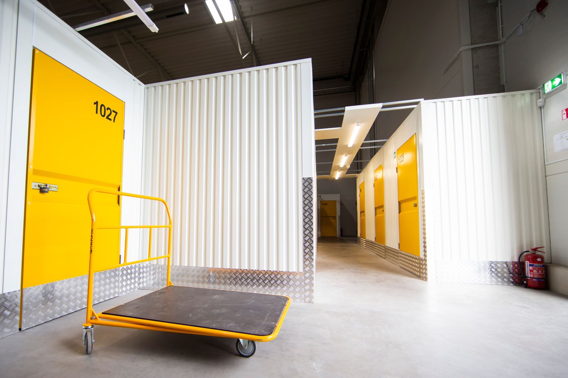 Bright yellow self-storage facility units with roll-up doors and a flatbed cart in a clean interior corridor.