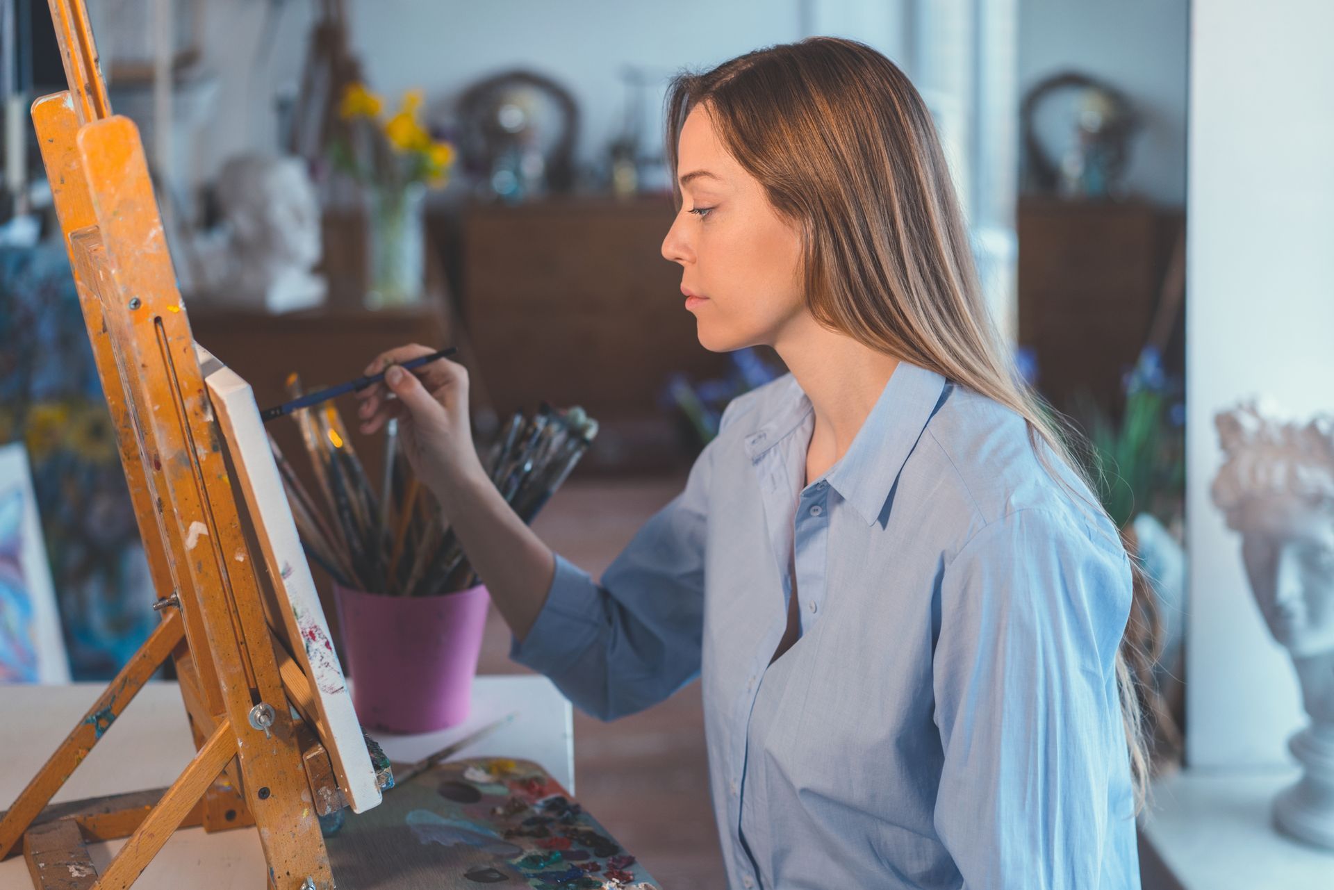 A woman is painting on a canvas on an easel.