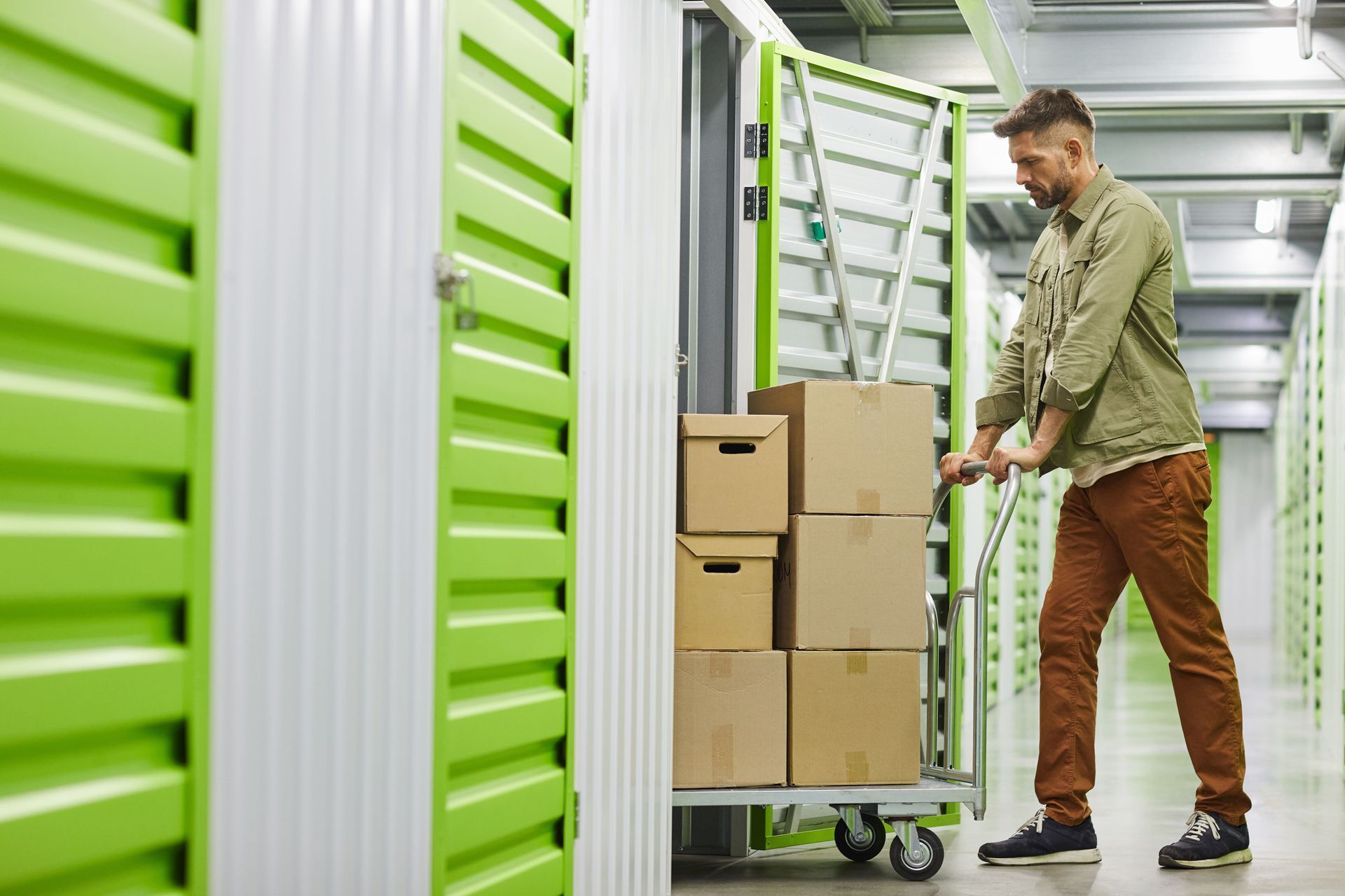 A man is pushing a cart filled with boxes in a storage room.
