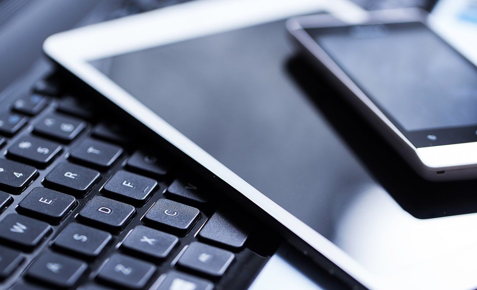 A tablet is laying on top of a keyboard next to a cell phone