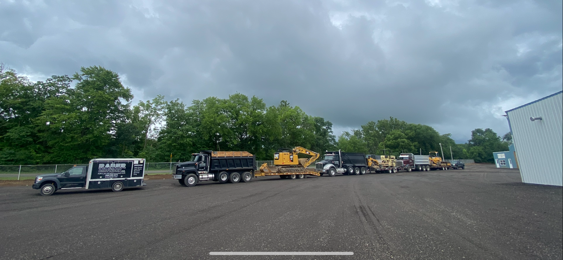 Line of heavy machinery and trucks parked outdoors under overcast skies.