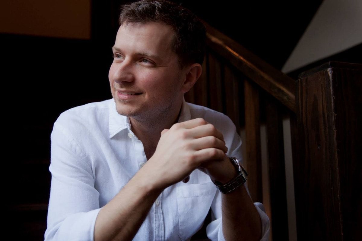 a man in a white shirt is sitting on a set of stairs with his hands folded .