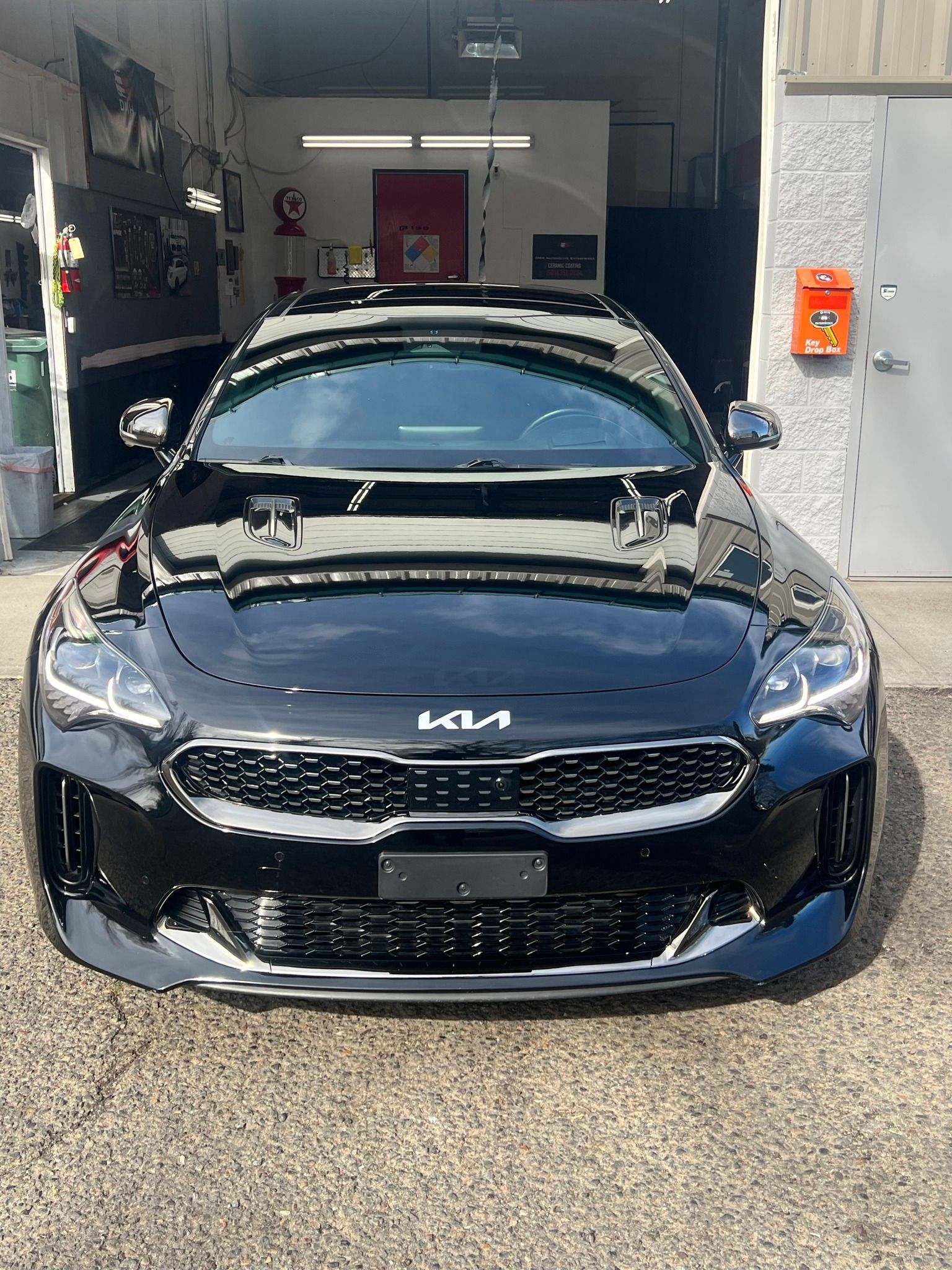 Black Kia sedan parked outside an auto shop garage, front view