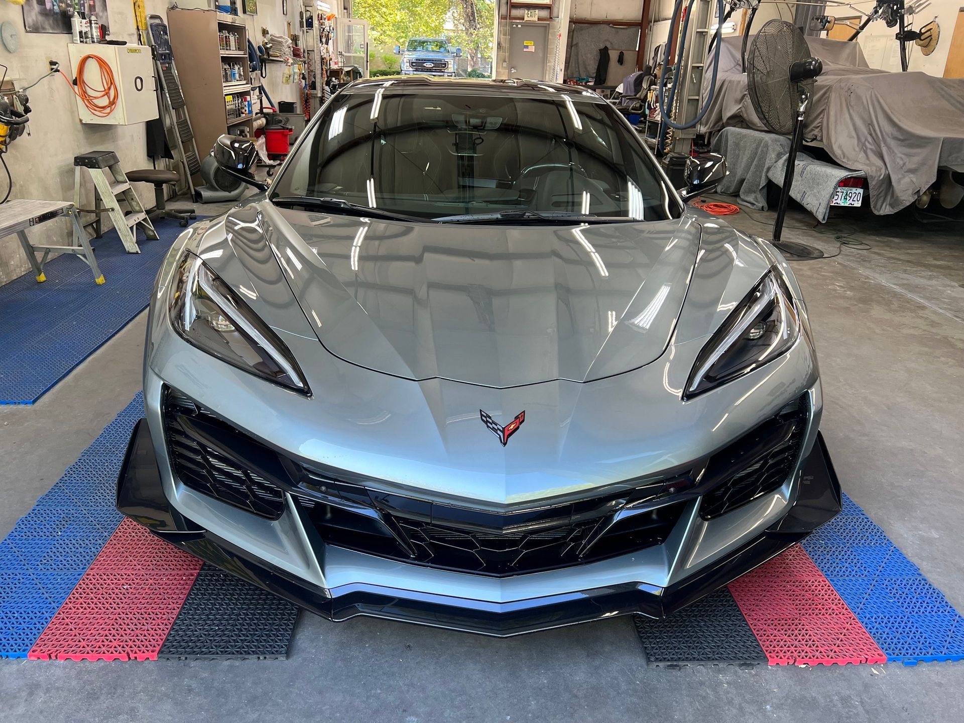 Silver sports car in a workshop, front view with glossy hood and angular headlights.