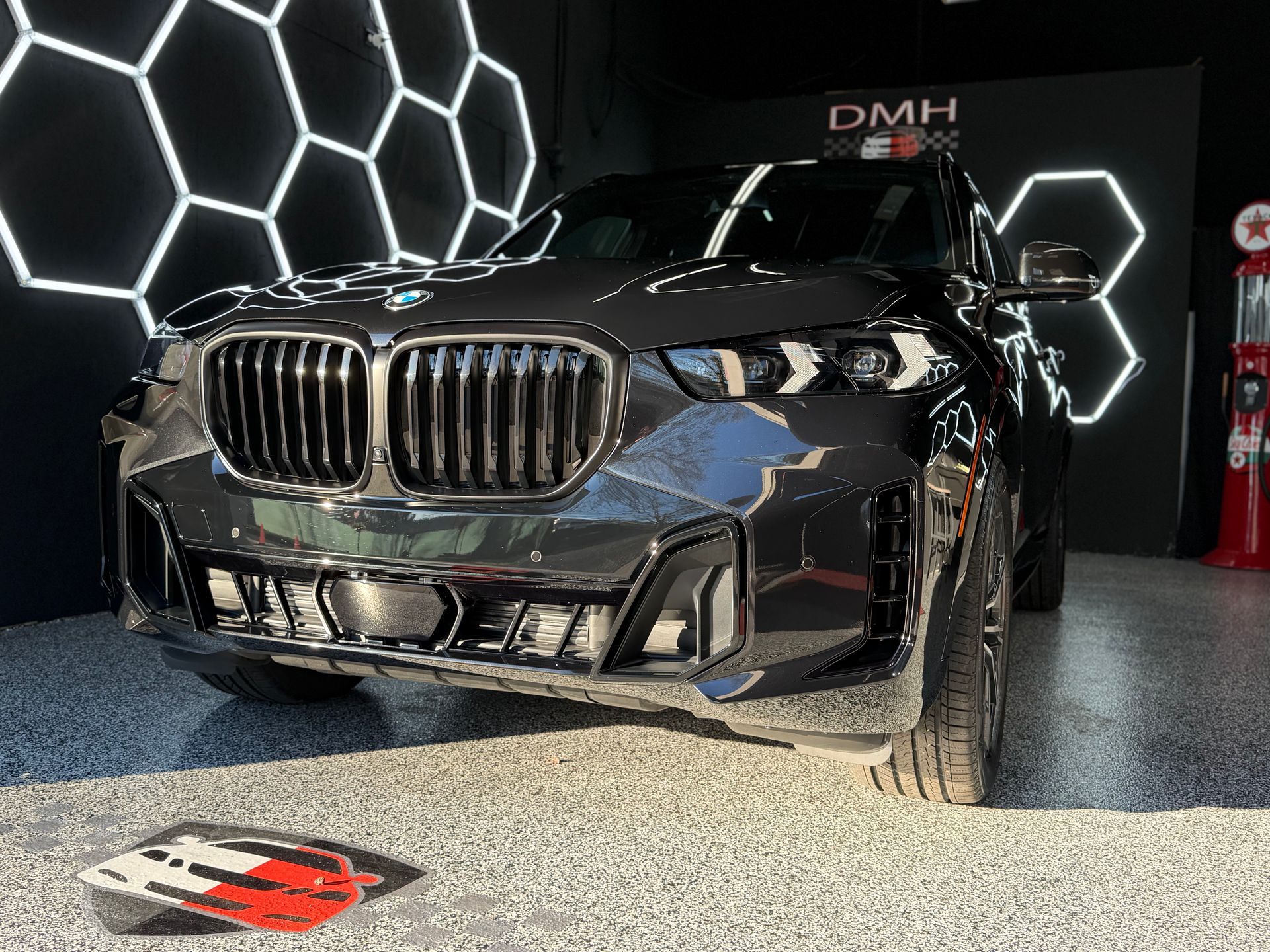 Black BMW SUV on display under hexagon lights at an auto show