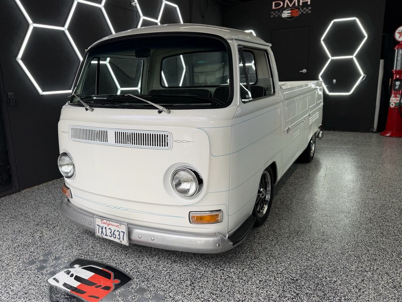 White vintage van on display in a showroom with hexagon wall lights and speckled floor