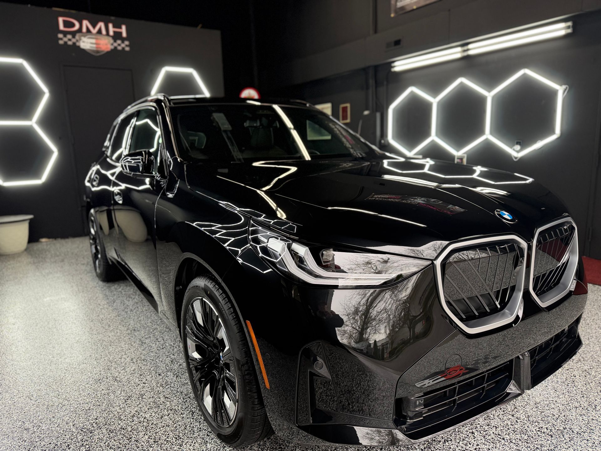 Black luxury SUV in a showroom with bright hexagonal wall lights.