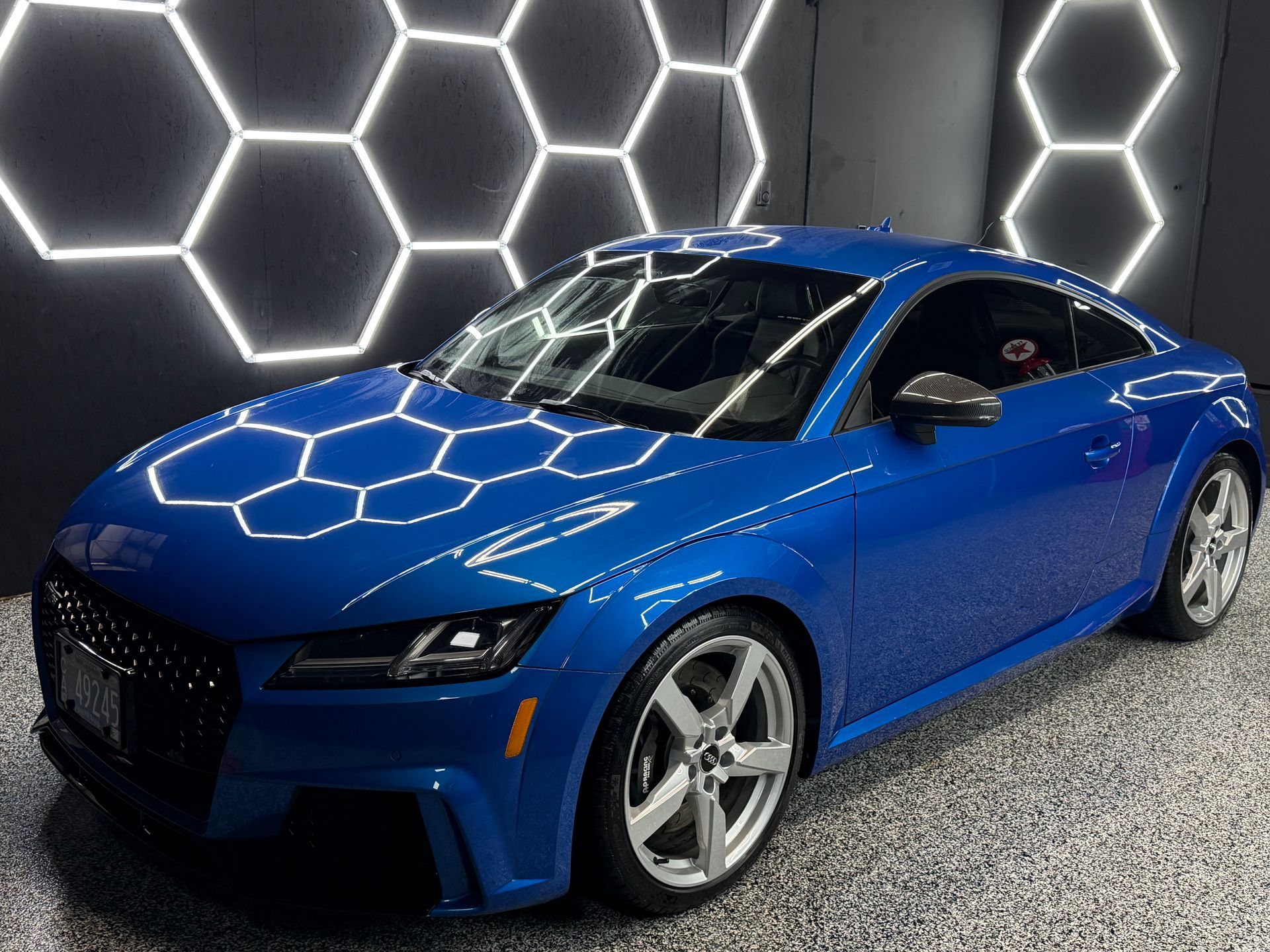 Blue sports coupe in a showroom, with hexagonal wall lights reflecting on the hood