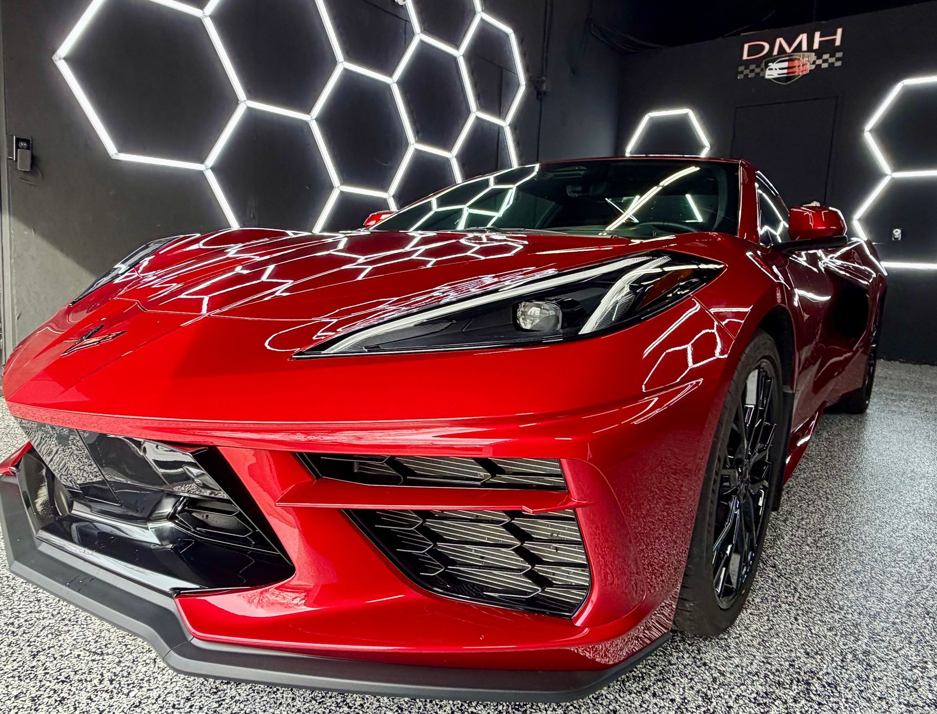 Red sports car displayed indoors under hexagonal lights, front-left view, glossy finish.