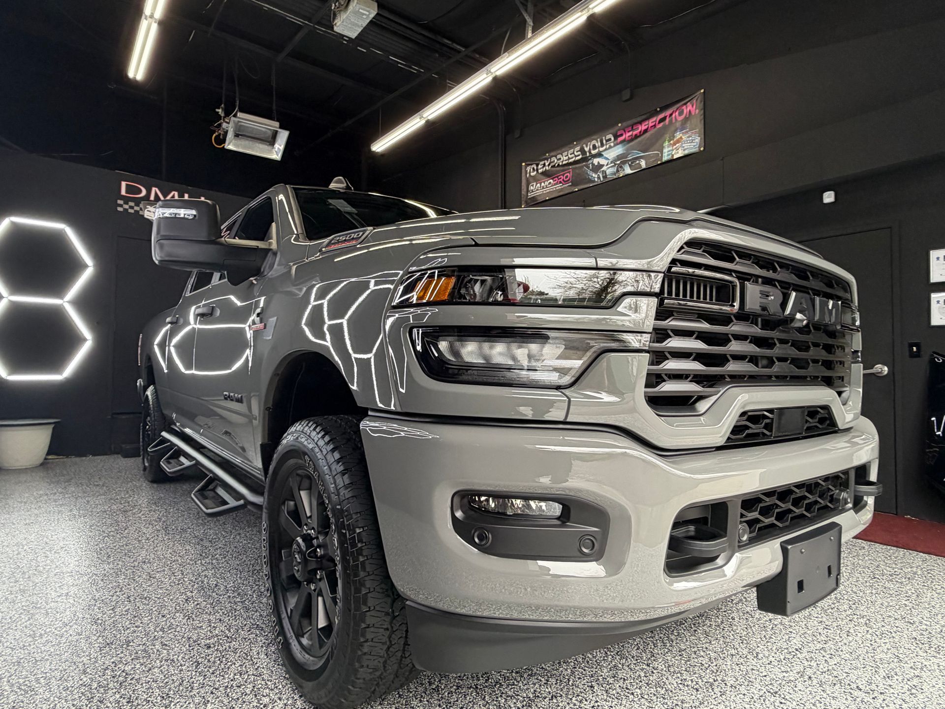 Gray pickup truck in a showroom, front three-quarter view with off-road tires and black wheels