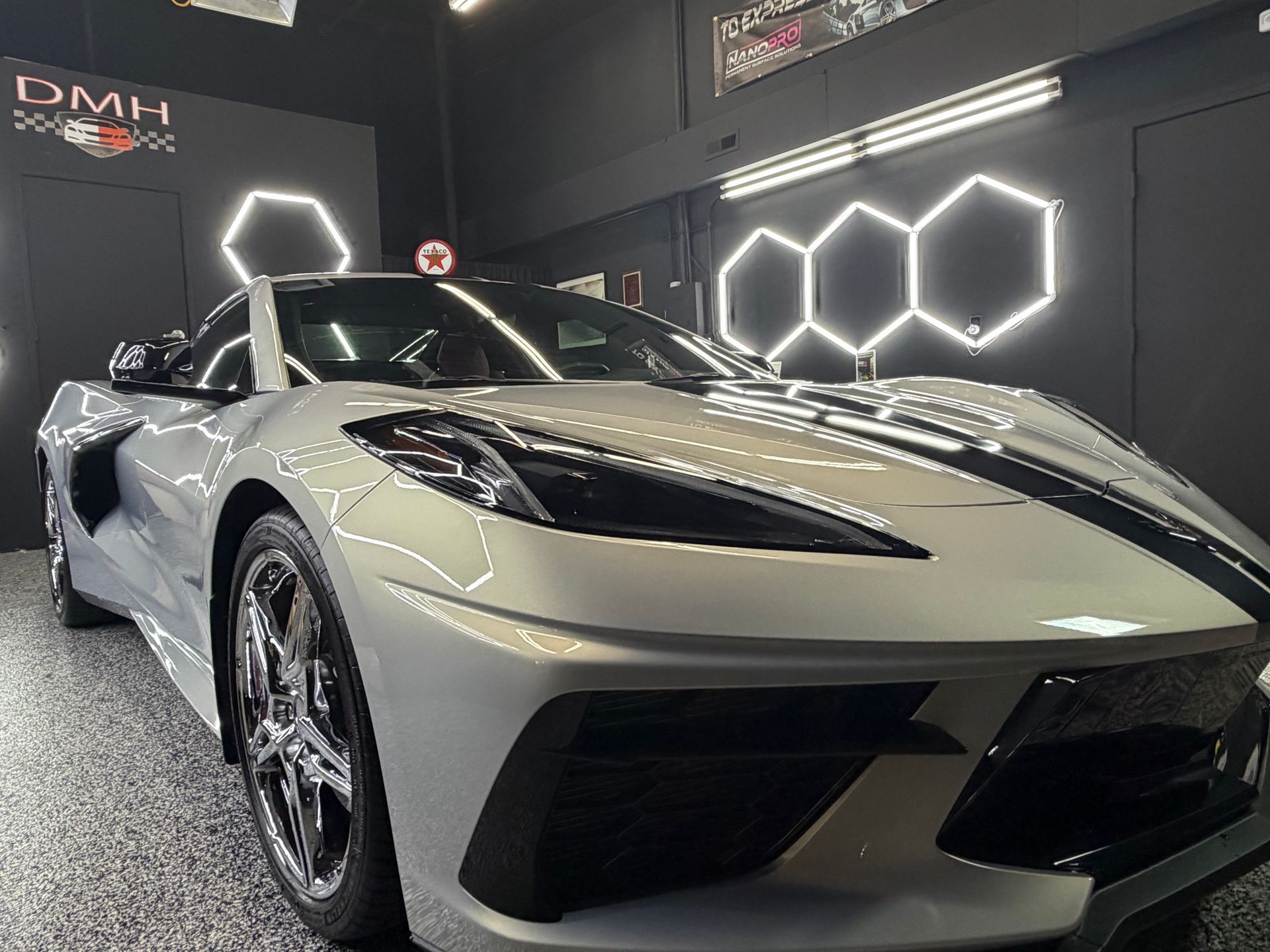 White sports car in a dim showroom with hexagonal wall lights and a reflective floor