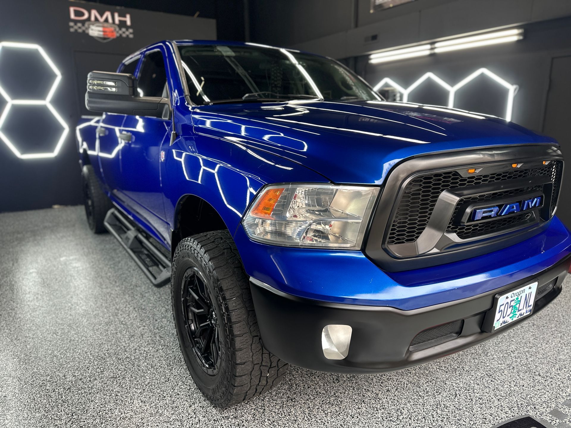Blue pickup truck displayed indoors under bright lights, with black wheels and chrome grille.