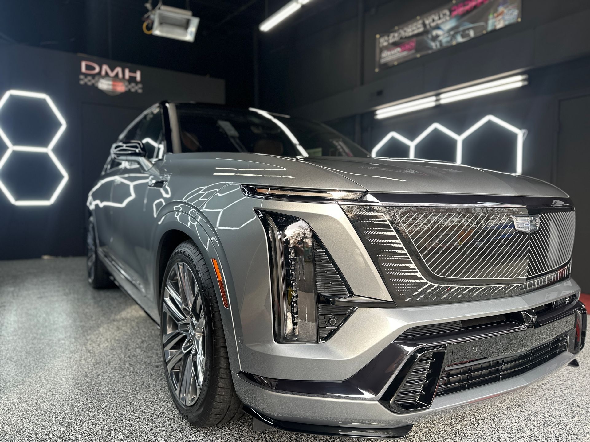 Silver luxury SUV in a showroom, viewed from the front-left under bright display lights.
